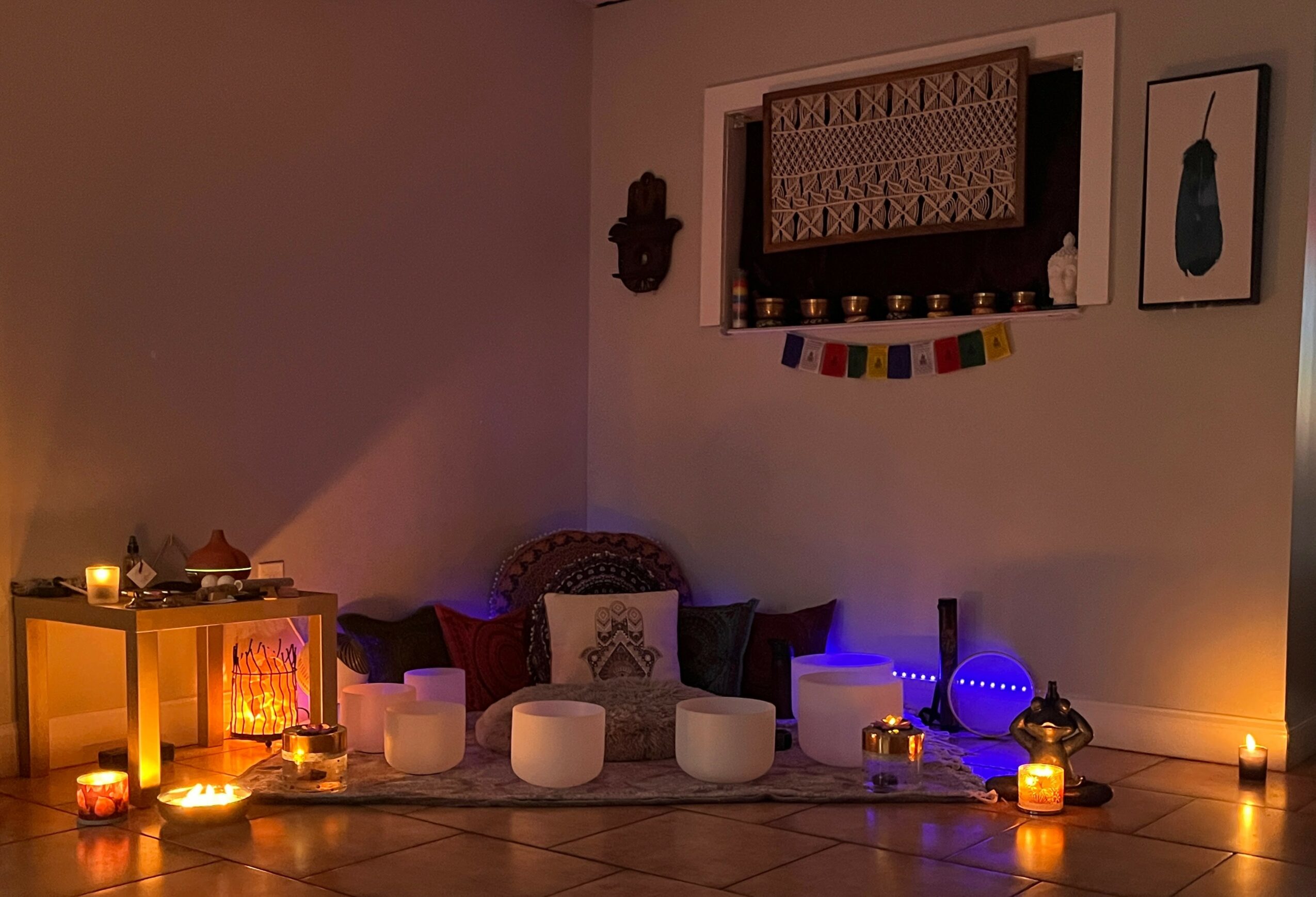 Indoor scene with candles, cushions, and decorative items on the floor, wall art, and a window with hanging decorations.