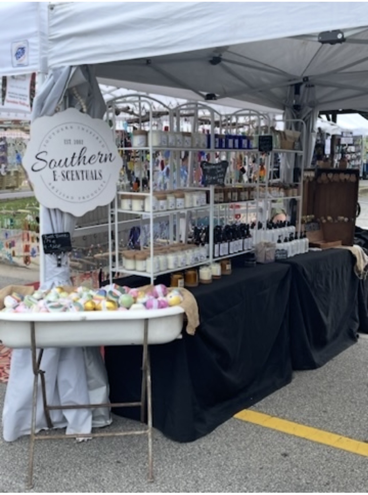 Vendor booth with jewelry and accessories displayed on shelves under a white canopy at an outdoor market.