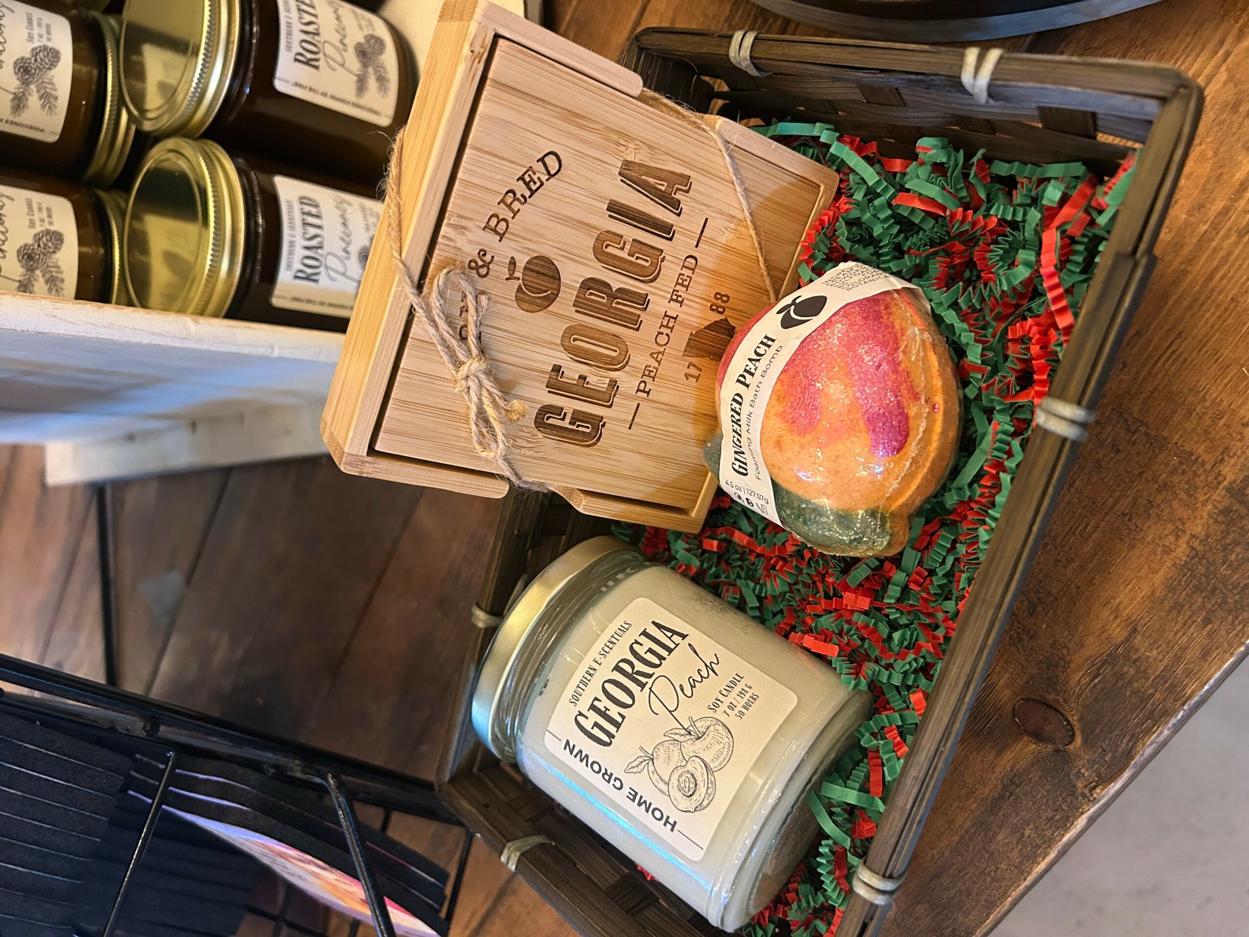 Gift box with a wooden sign, apple-shaped candle, and a candle jar, decorated with red and green shredded paper.