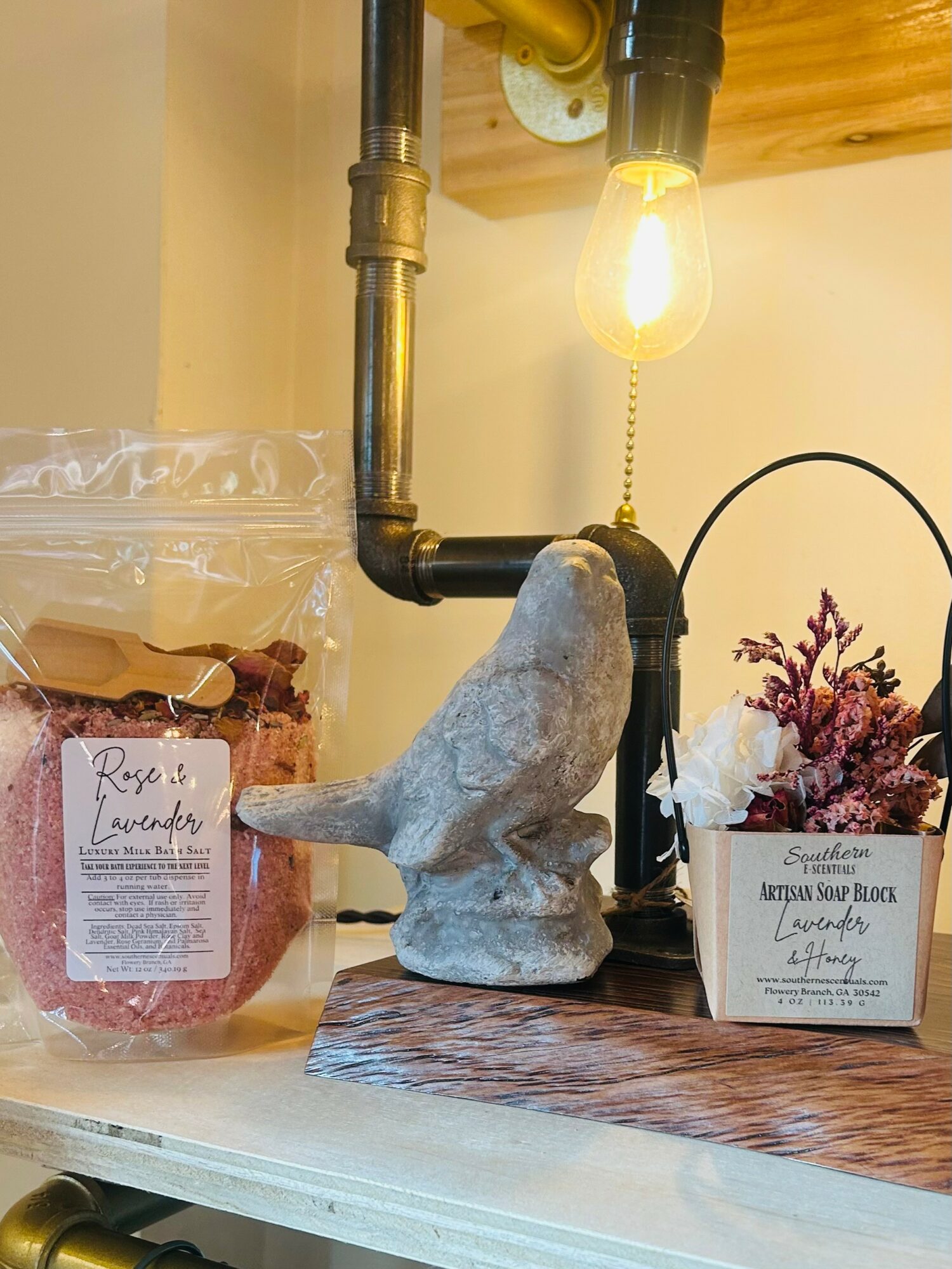 Decorative elephant sculpture with a light bulb hanging above, a jar of dried roses, and a small floral arrangement on a wooden surface.