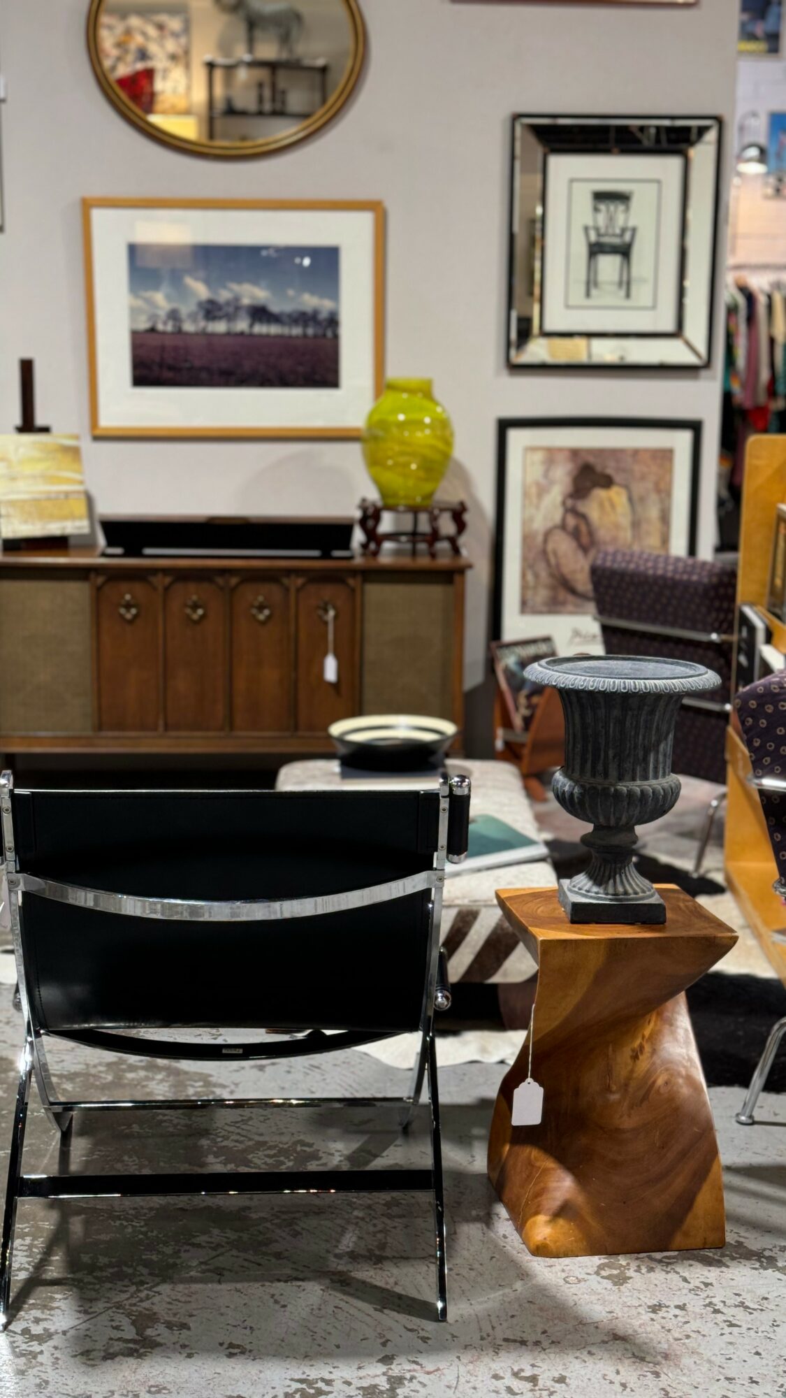 Interior room with framed artwork on wall, wooden sideboard, and chairs around a table, with decorative objects including a yellow vase.