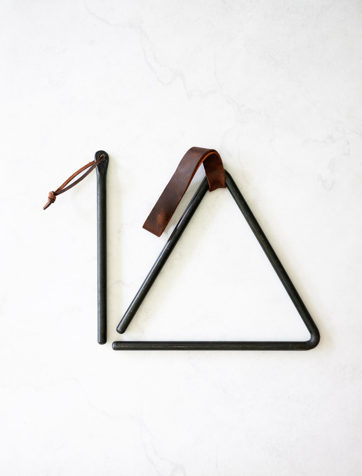 A black metal triangle with a brown leather strap, a black stick with a string, and a black stick with a loop, on a white surface.