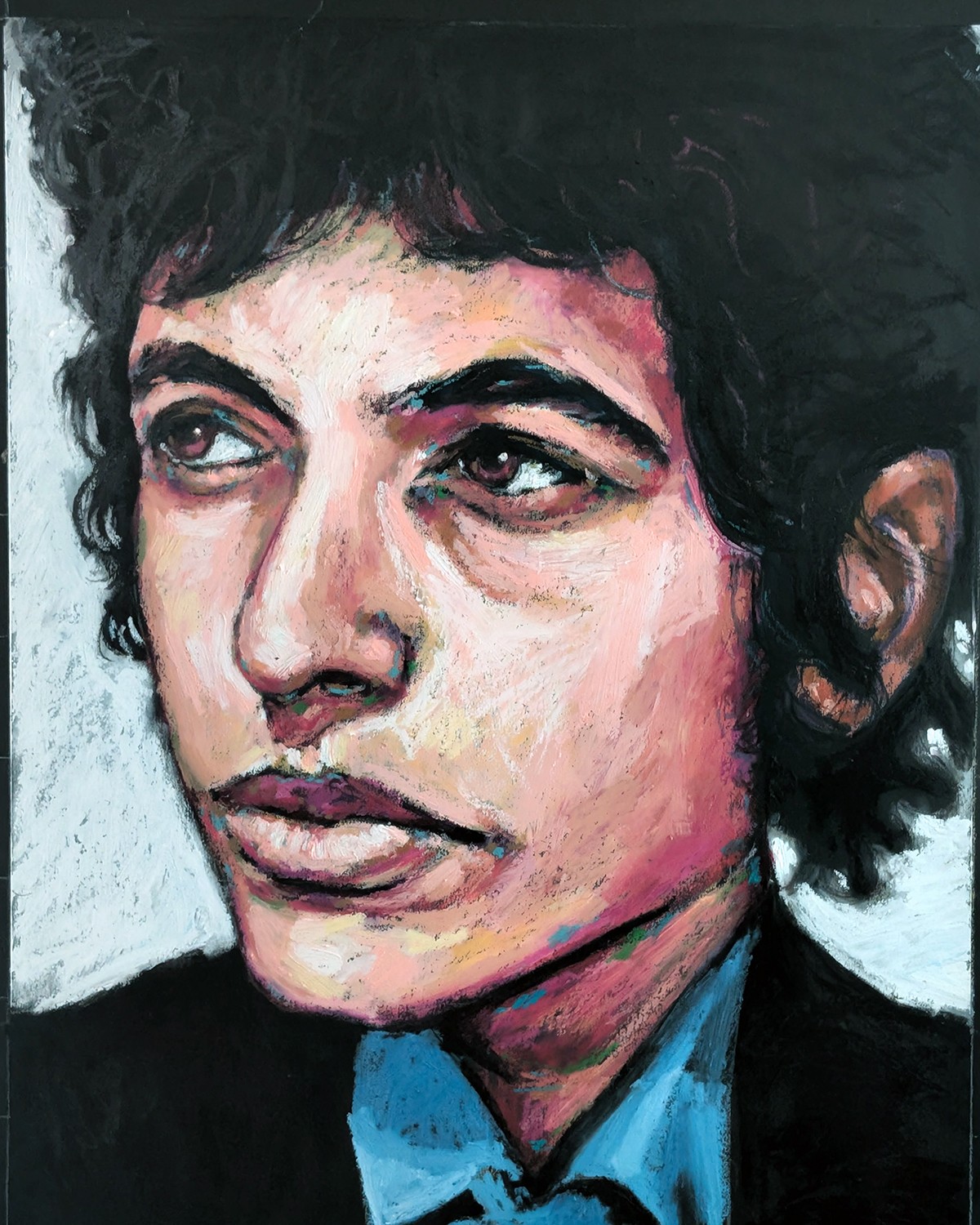 Portrait of a person with short, dark, curly hair, wearing a blue shirt and black jacket, looking to the side.