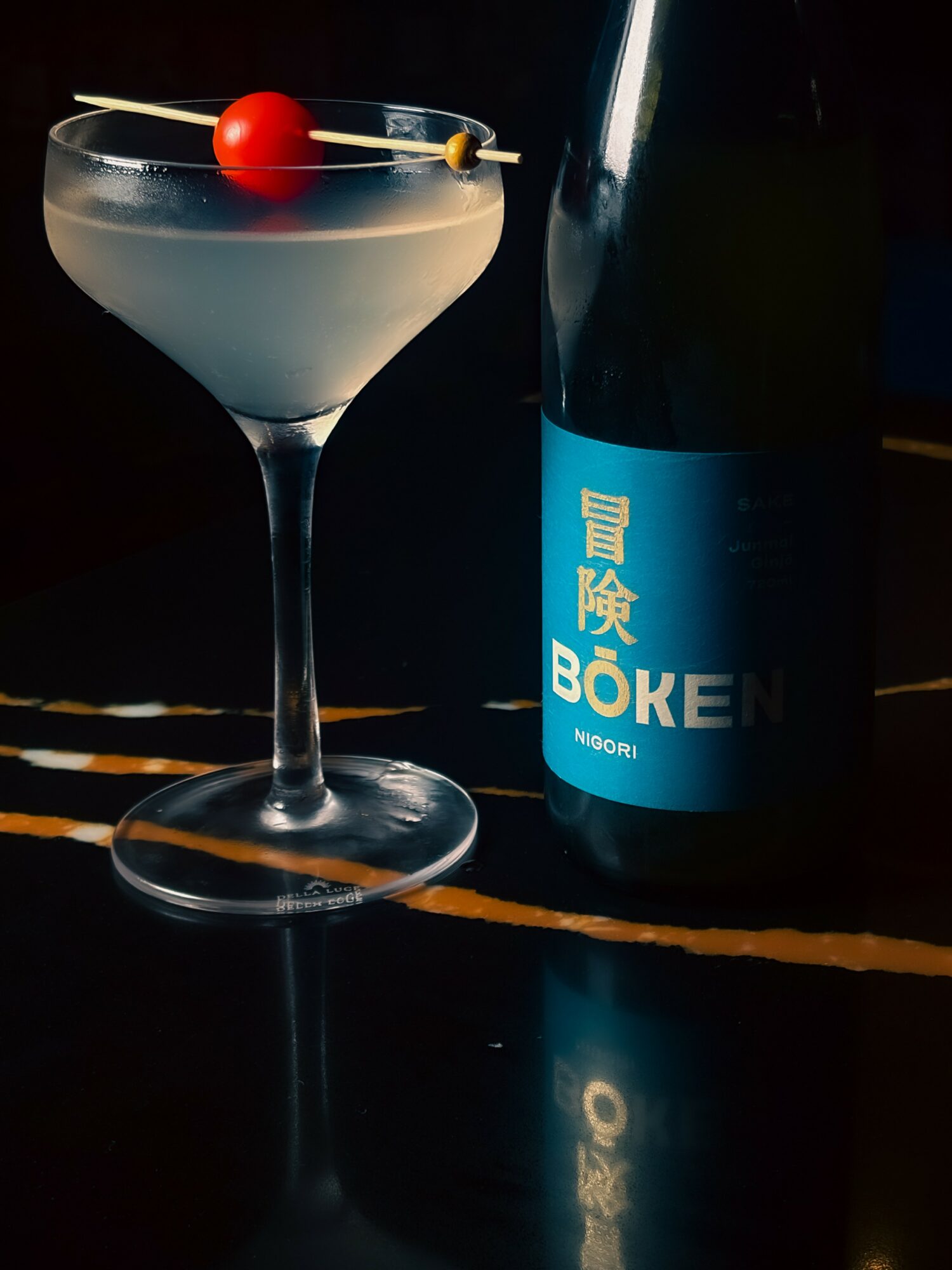 Cocktail glass with a cherry and a bottle with Japanese text on a dark background.
