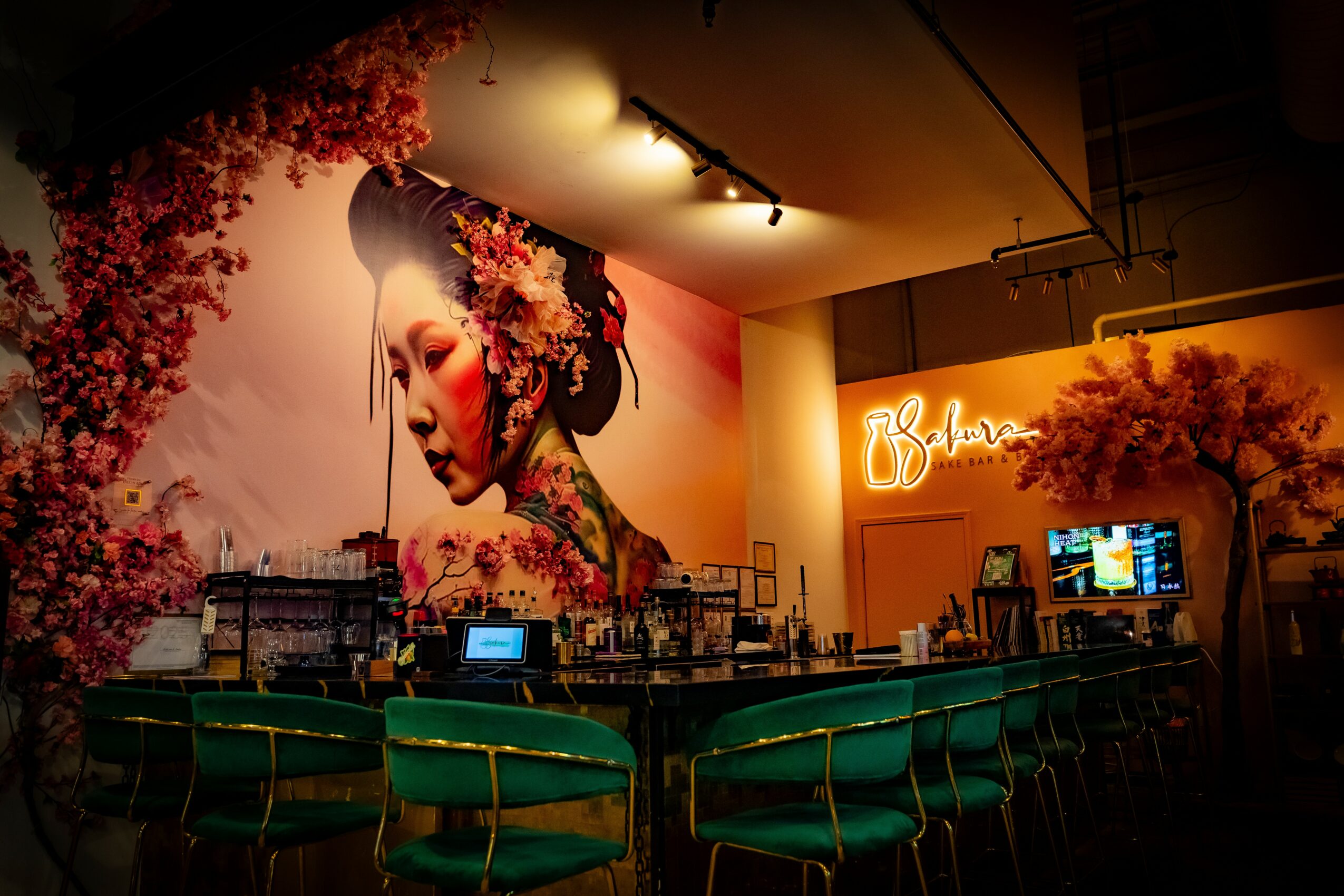Interior of a cafe with a large mural of a woman with flowers in her hair, green chairs, and warm lighting.