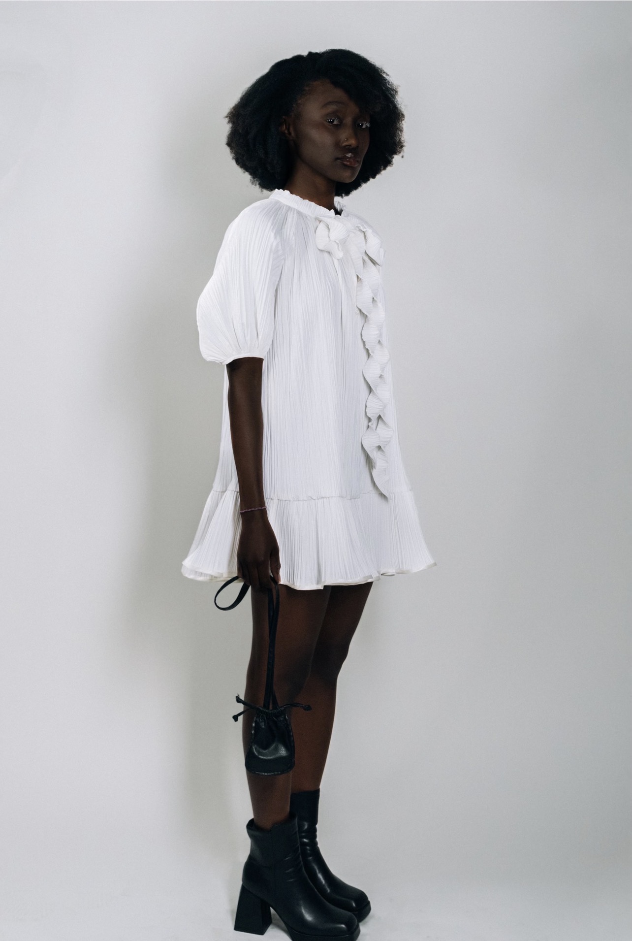 Woman in white dress with puffed sleeves and ruffles, standing against a plain background.