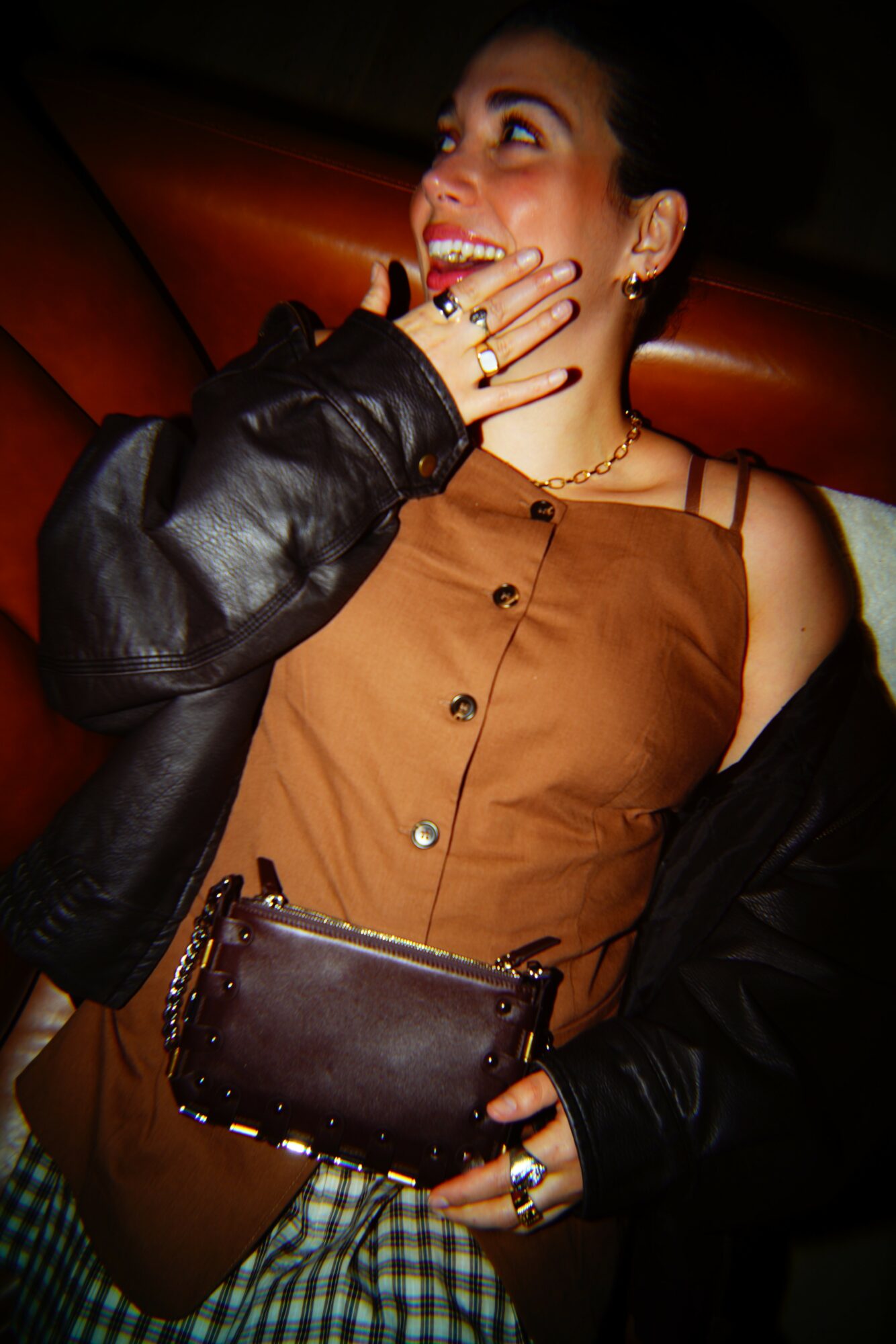 Woman smiling, wearing a brown top, holding a small purse, with a black jacket partially on her arm.