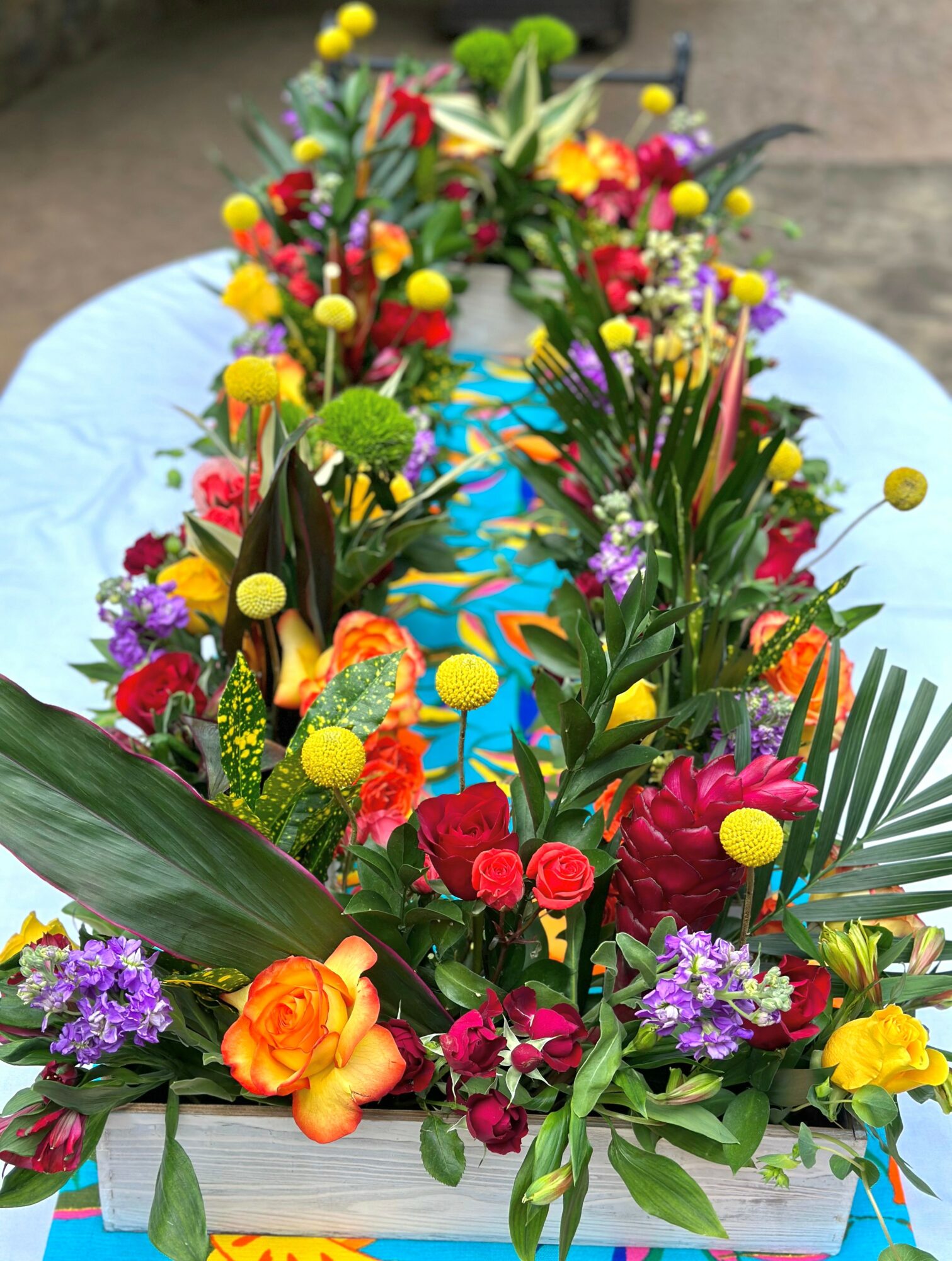 Colorful flower arrangement with various flowers and greenery on a table, viewed from above.