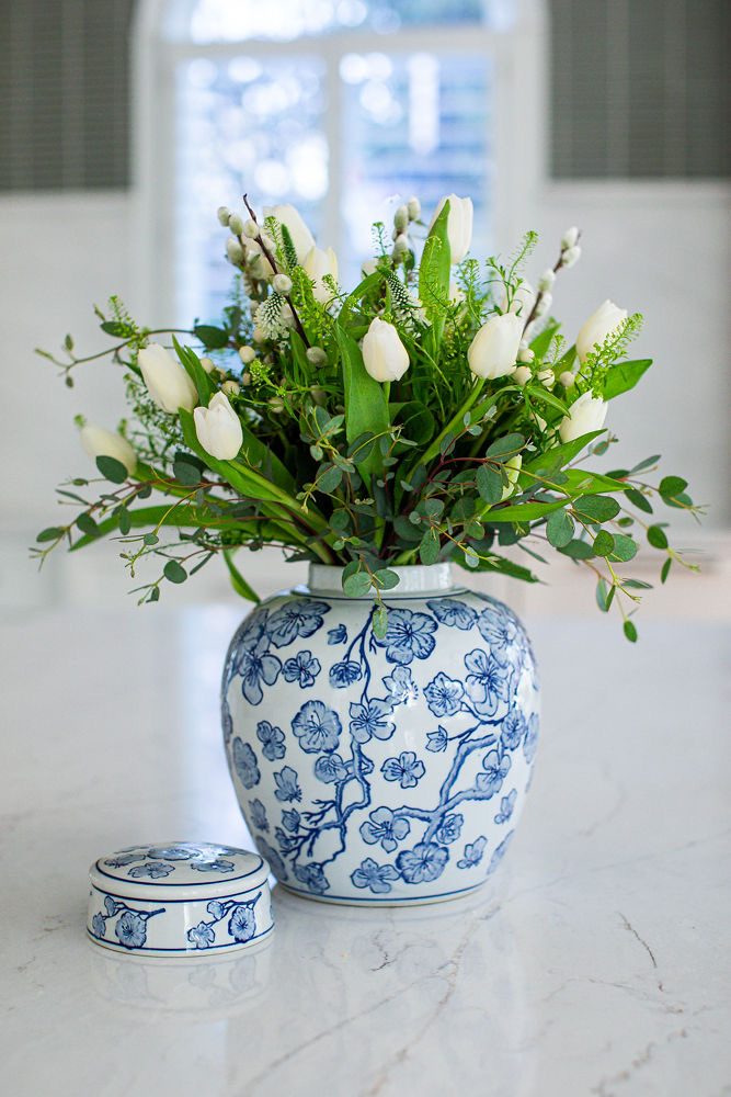 Flower arrangement with white tulips and greenery in a blue and white patterned vase on a white surface.
