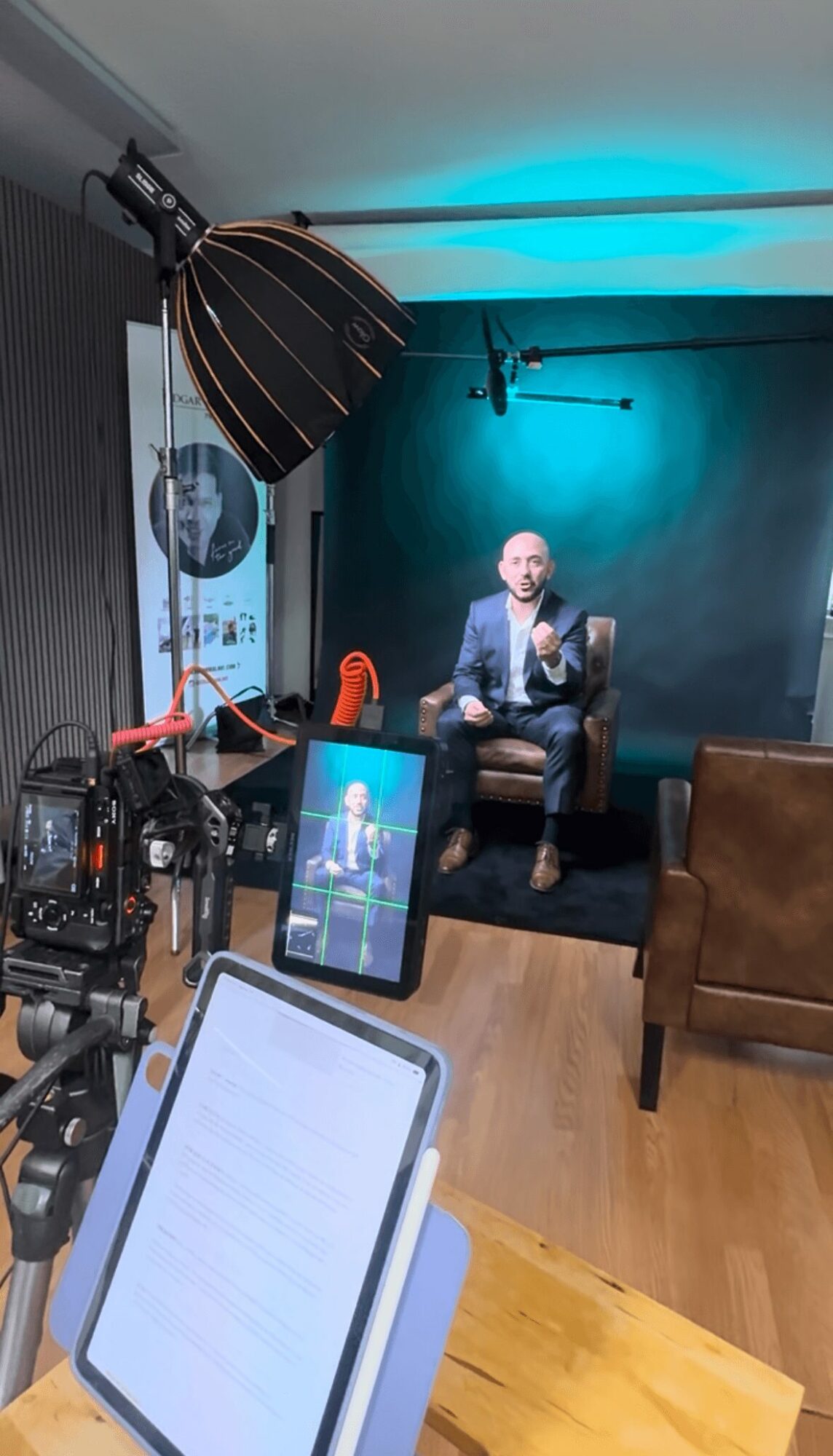 Person sitting on a chair in a photography studio with professional lighting and equipment, blue backdrop, and a tablet on a table.