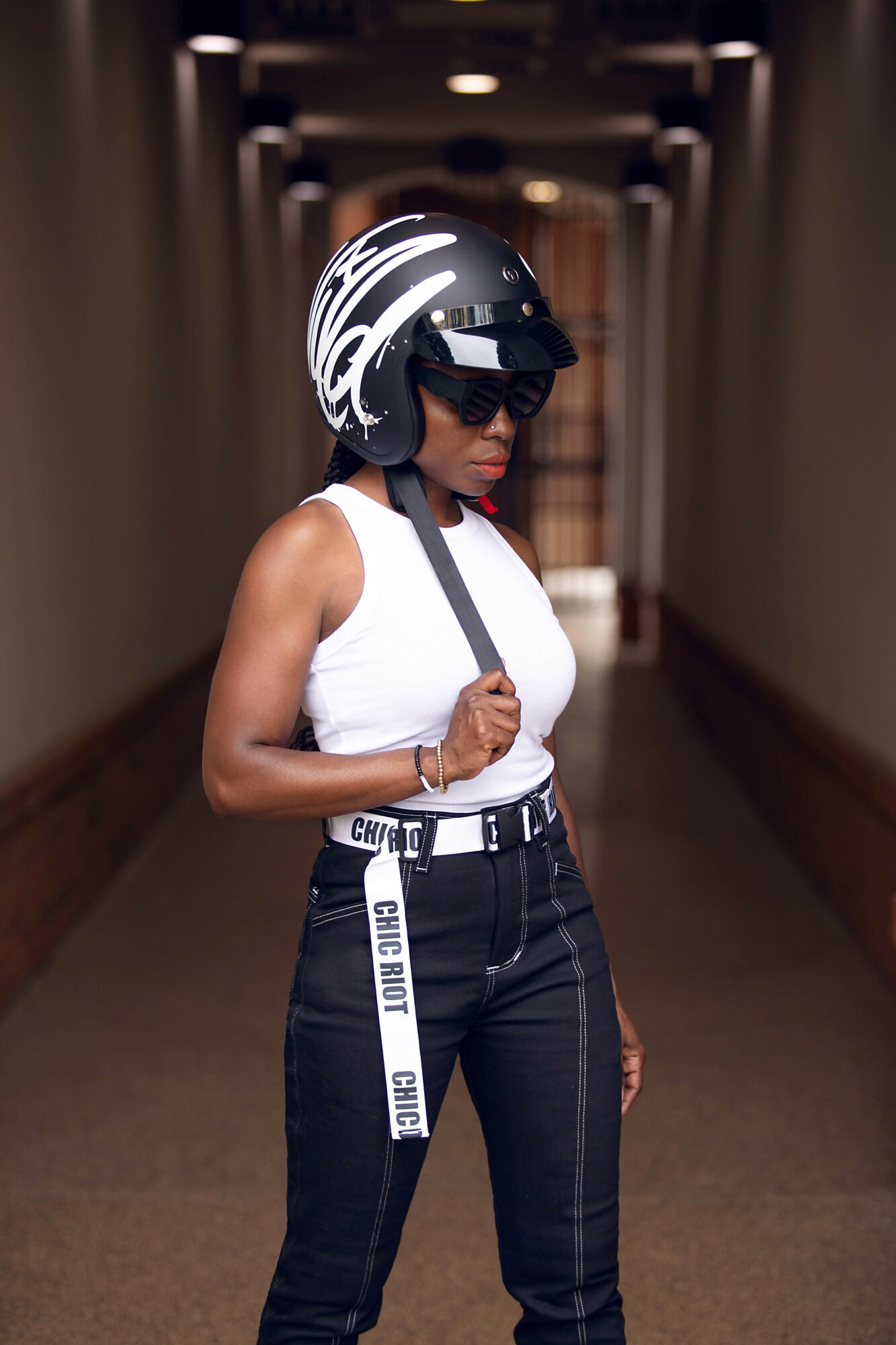 Woman wearing a helmet, sunglasses, and a white tank top standing in a hallway.