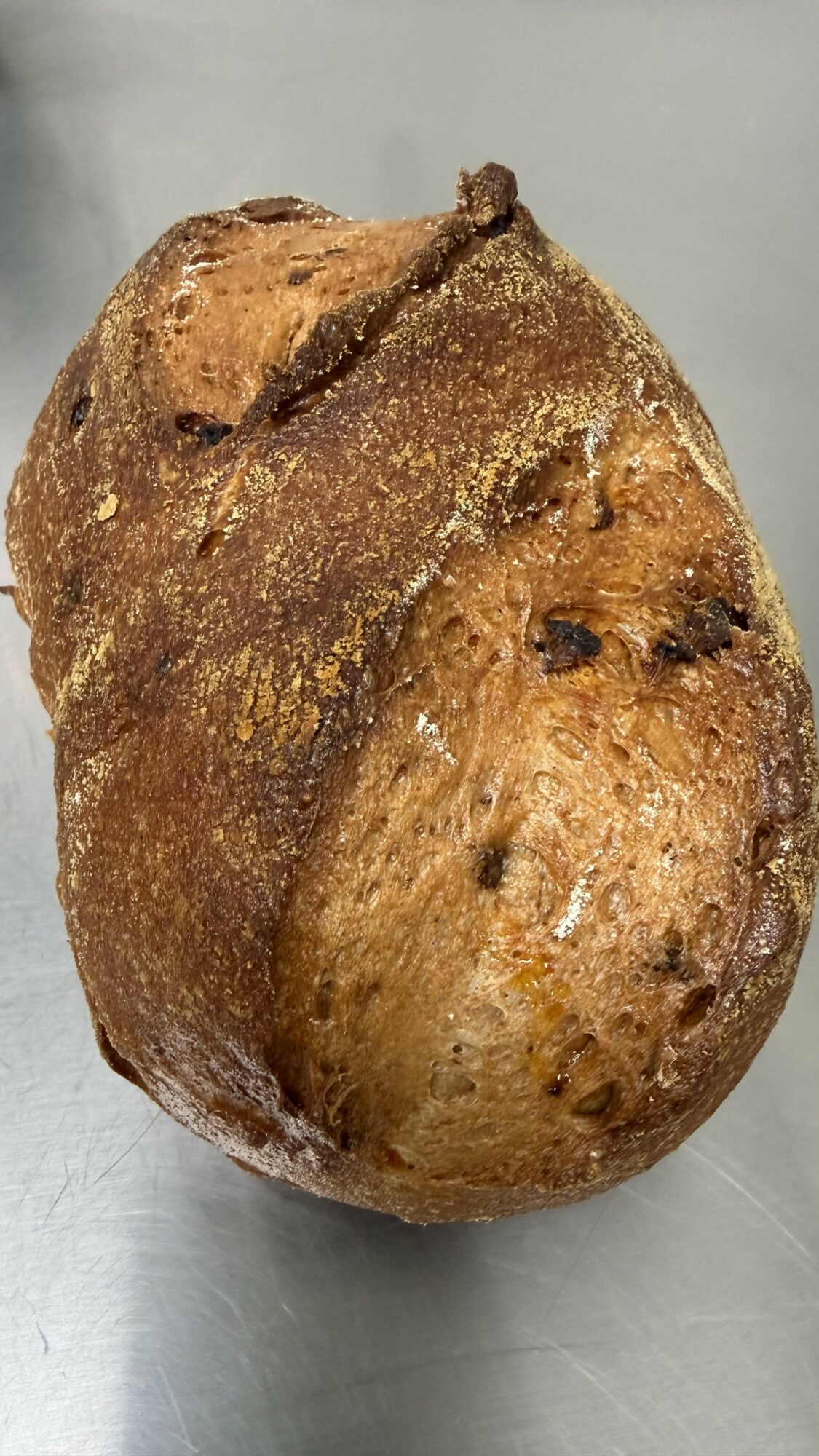 Baked potato with a rough, textured surface and some dark spots, placed on a flat surface.