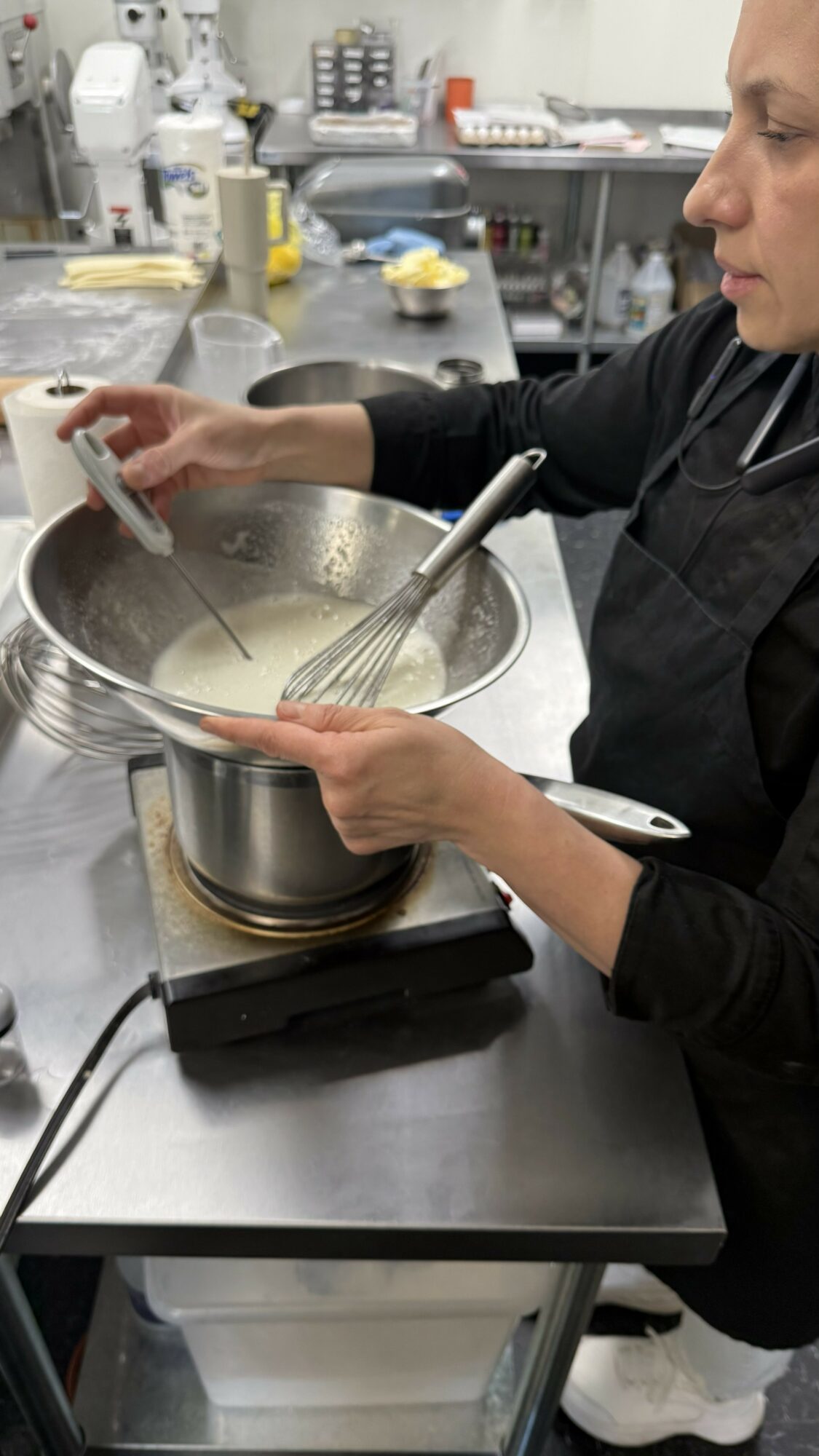 Person stirring a mixture in a large metal bowl on a kitchen counter, with various utensils and supplies in the background.