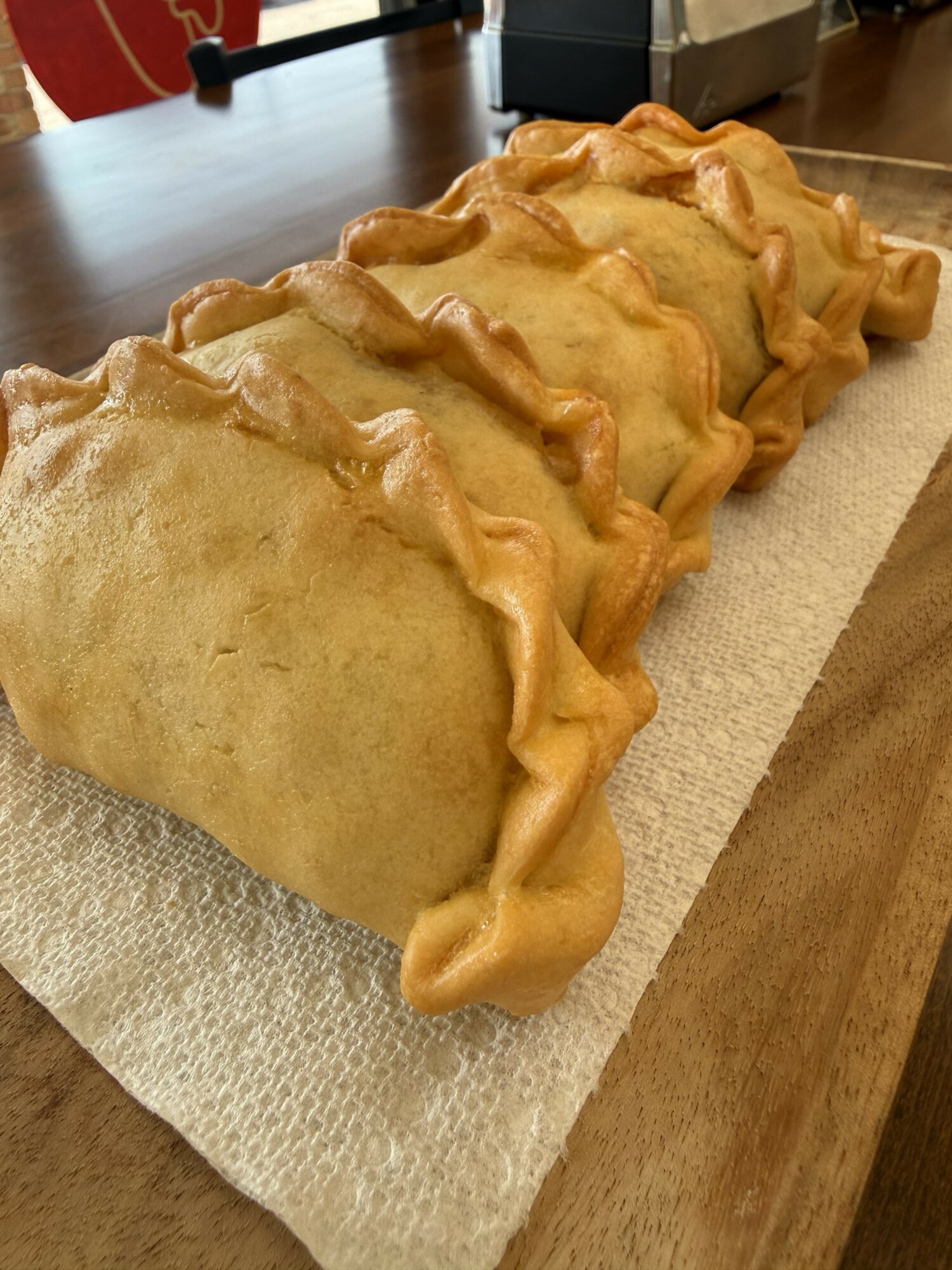Four baked calzones with golden crust and crimped edges on a paper towel on a wooden table.