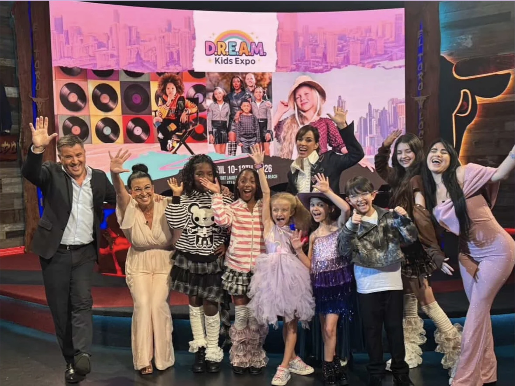 Group of children and adults smiling and posing in front of a colorful Kids Expo backdrop.