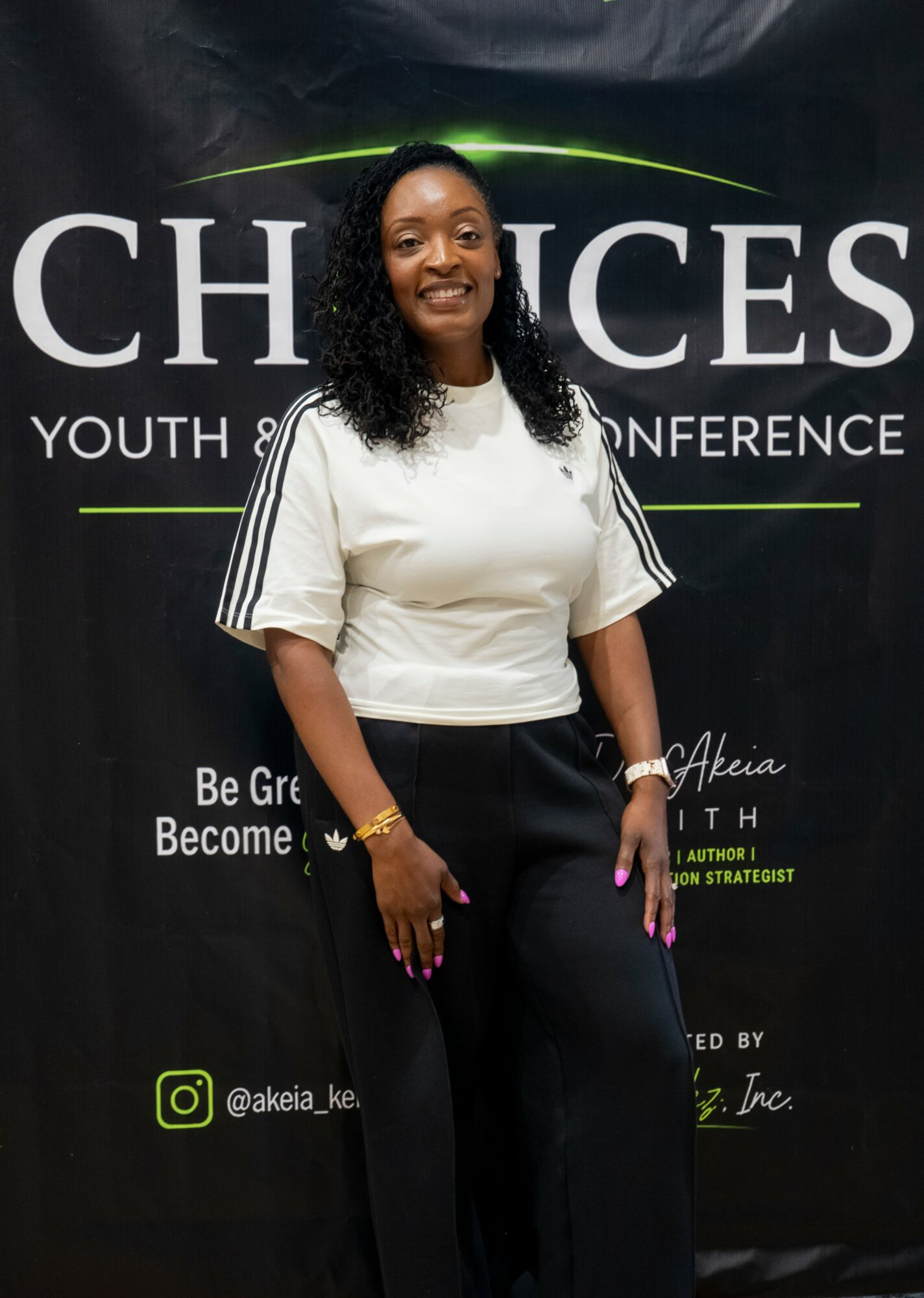 Smiling woman standing in front of a black conference backdrop with white text, wearing a white top and black pants.