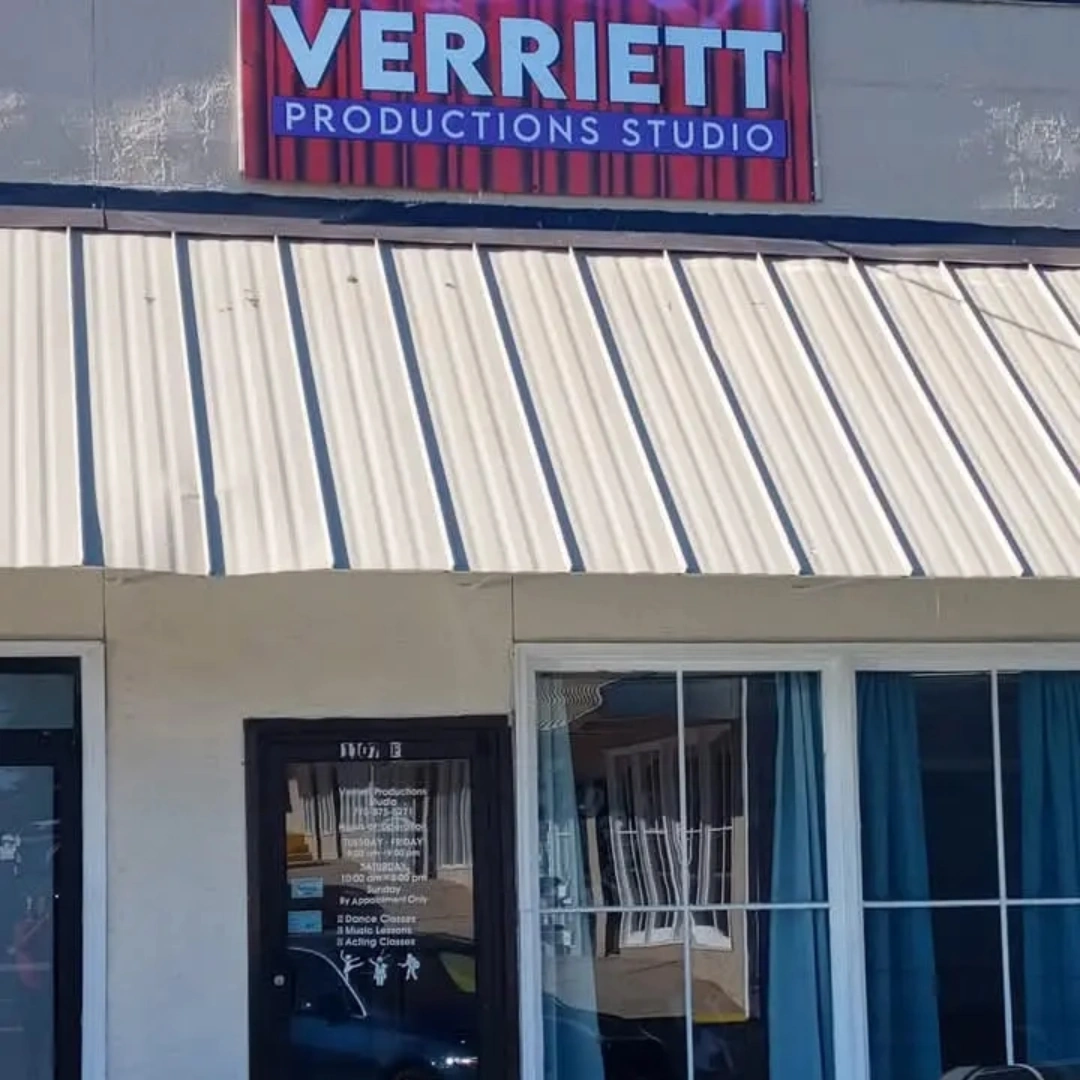 Building with a sign that reads 'VERRITT PRODUCTIONS STUDIO' and a window with blue curtains.