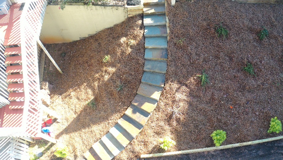 A curved pathway with steps in a yard, surrounded by gravel and small plants, viewed from above.