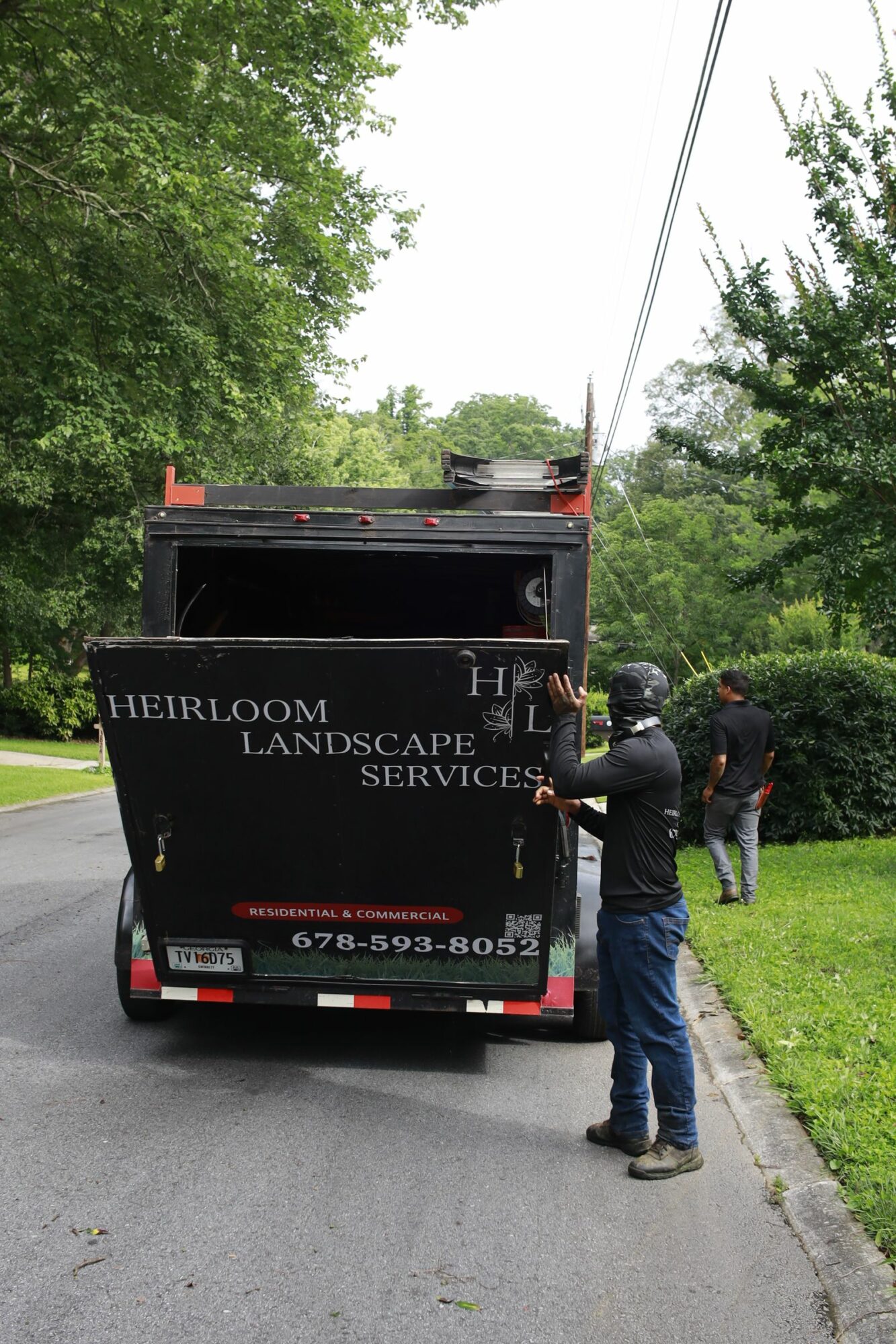 Person standing next to a black truck with a sign reading 'Herb Room & Spa' parked on a street with green trees.