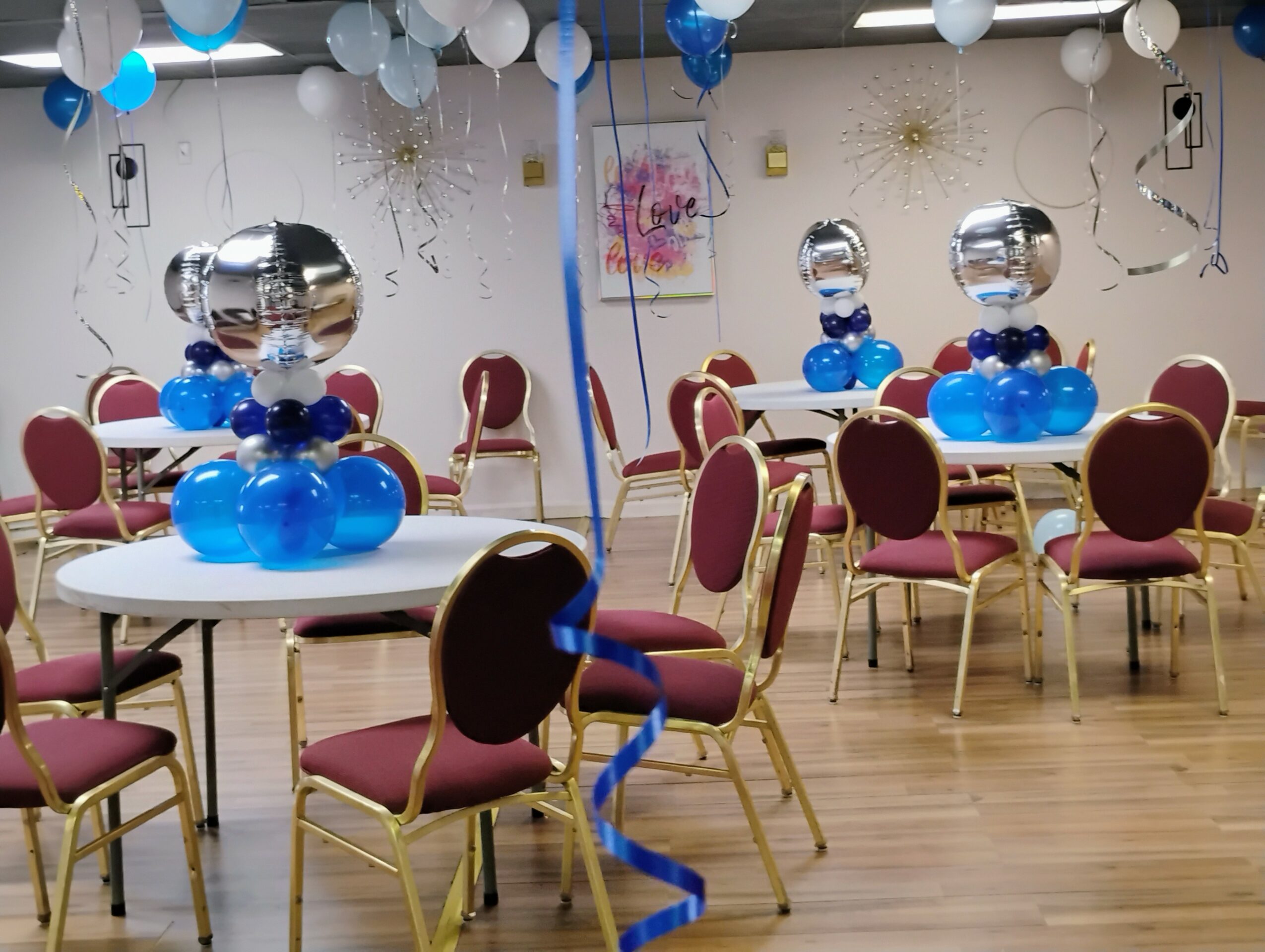 Party room decorated with balloons, tables, and chairs, with balloons and streamers hanging from the ceiling.
