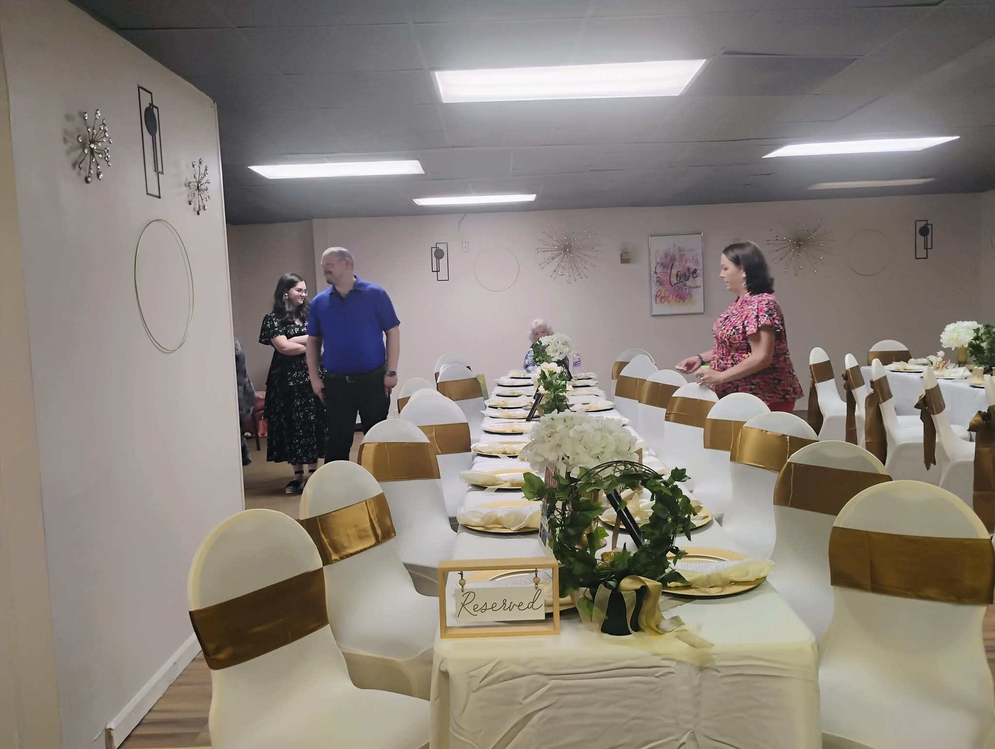 People standing and talking in a decorated banquet hall with tables set for an event.