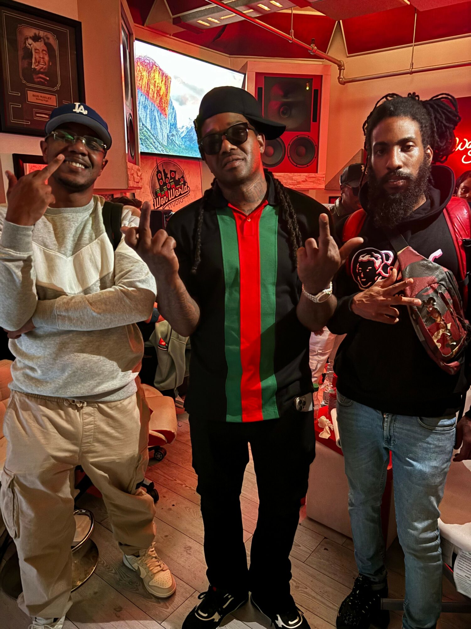 Three people posing indoors, one making a peace sign, two smiling, in a room with red and orange decor.