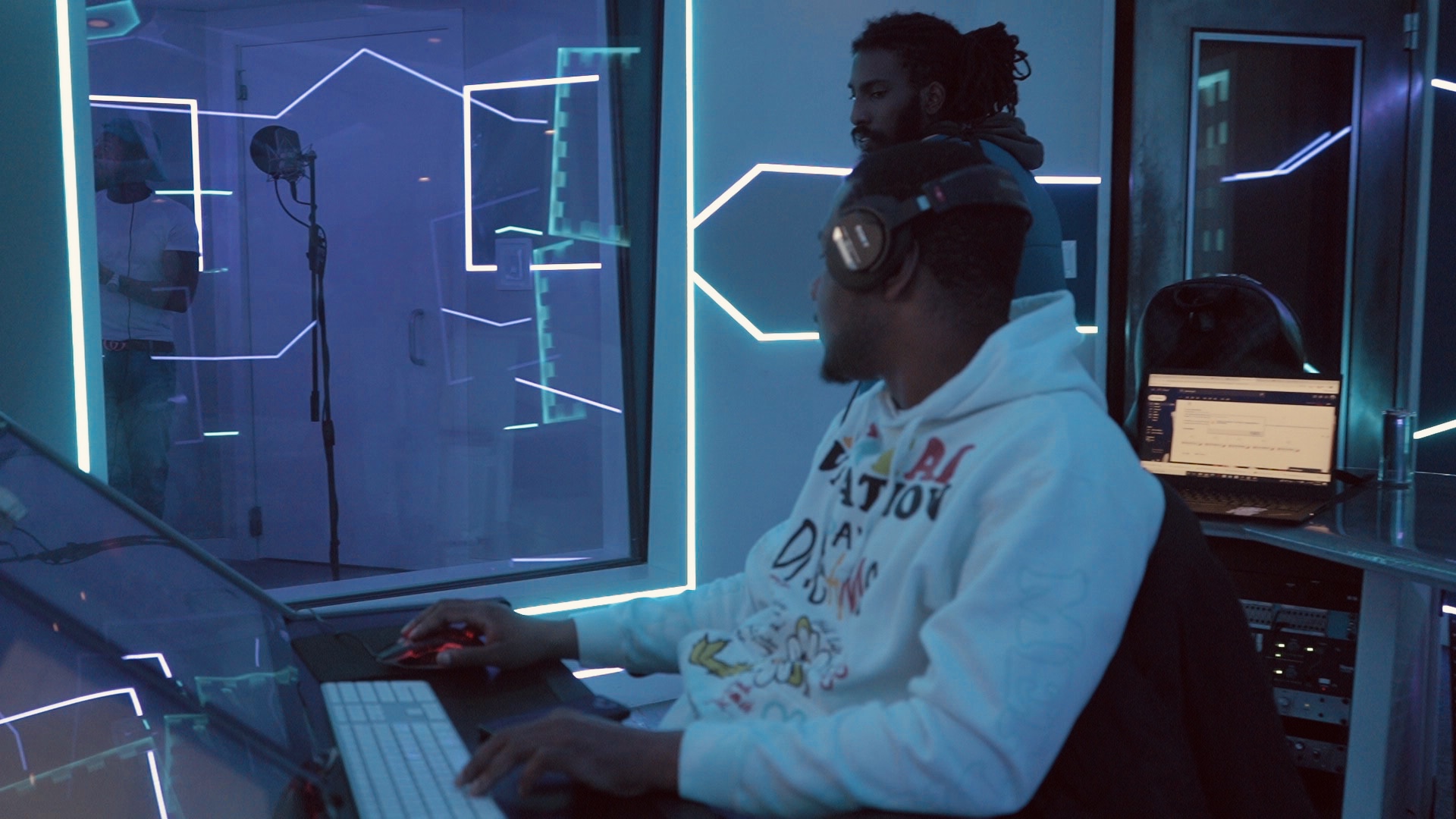 Person working at a computer in a futuristic, neon-lit room with reflective surfaces.