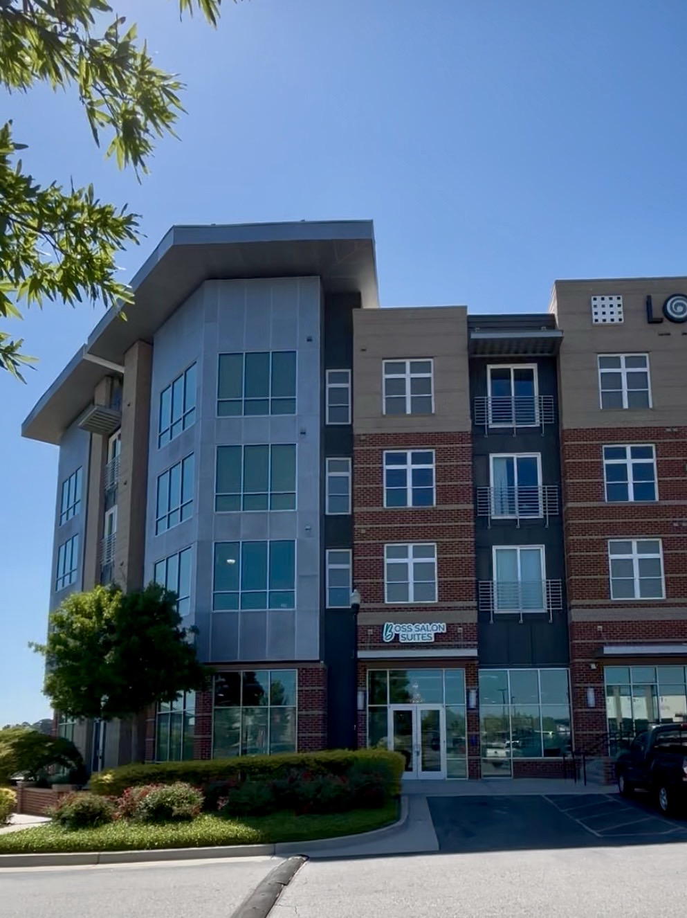 Modern multi-story building with glass windows and brick facade, under a clear blue sky, with trees and landscaping in front.