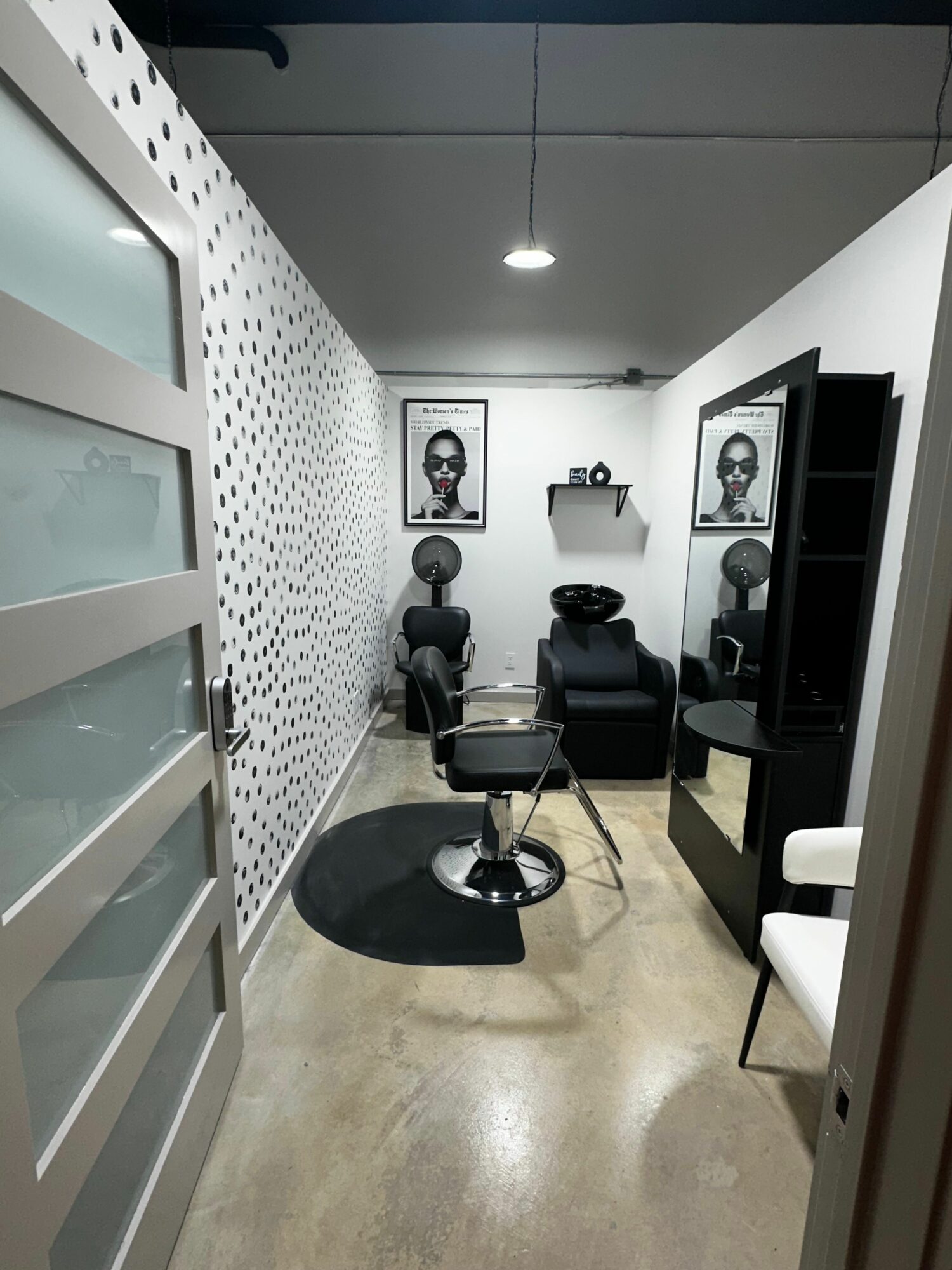Salon with hair styling chairs, mirrors, and shelves, viewed from an angle with a patterned wall and concrete floor.