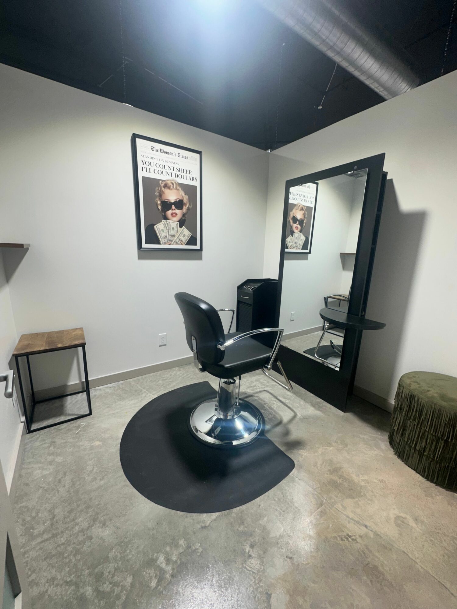Salon chair in front of a mirror with framed pictures on the wall, on a concrete floor.
