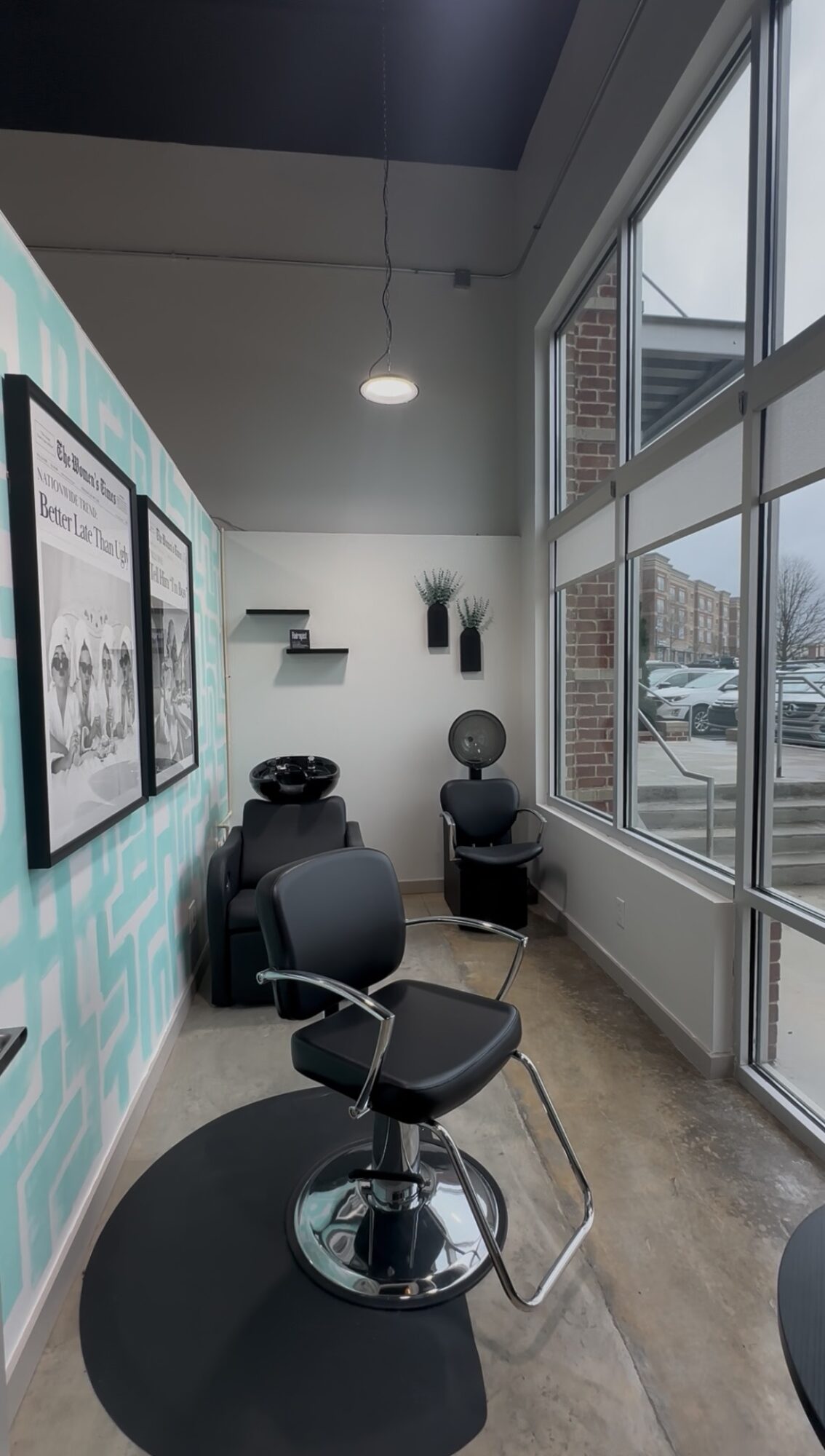 Salon interior with chairs, large windows, and wall decorations, illuminated by natural light, with a view of outside buildings.