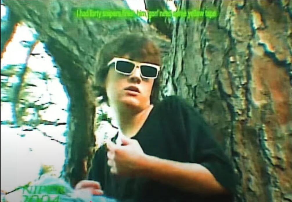 Person with sunglasses leaning against a tree outdoors, wearing a black shirt, with green text overlay.