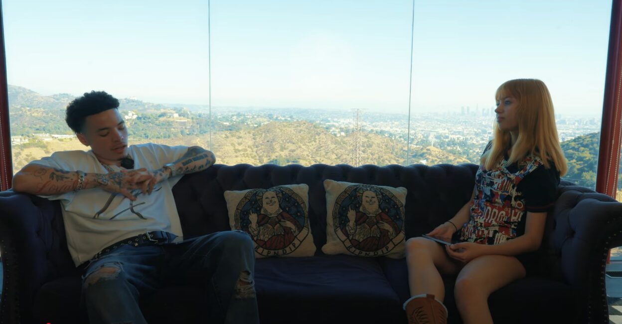 Two people sitting on a sofa in front of a large window with a city view, engaged in conversation.