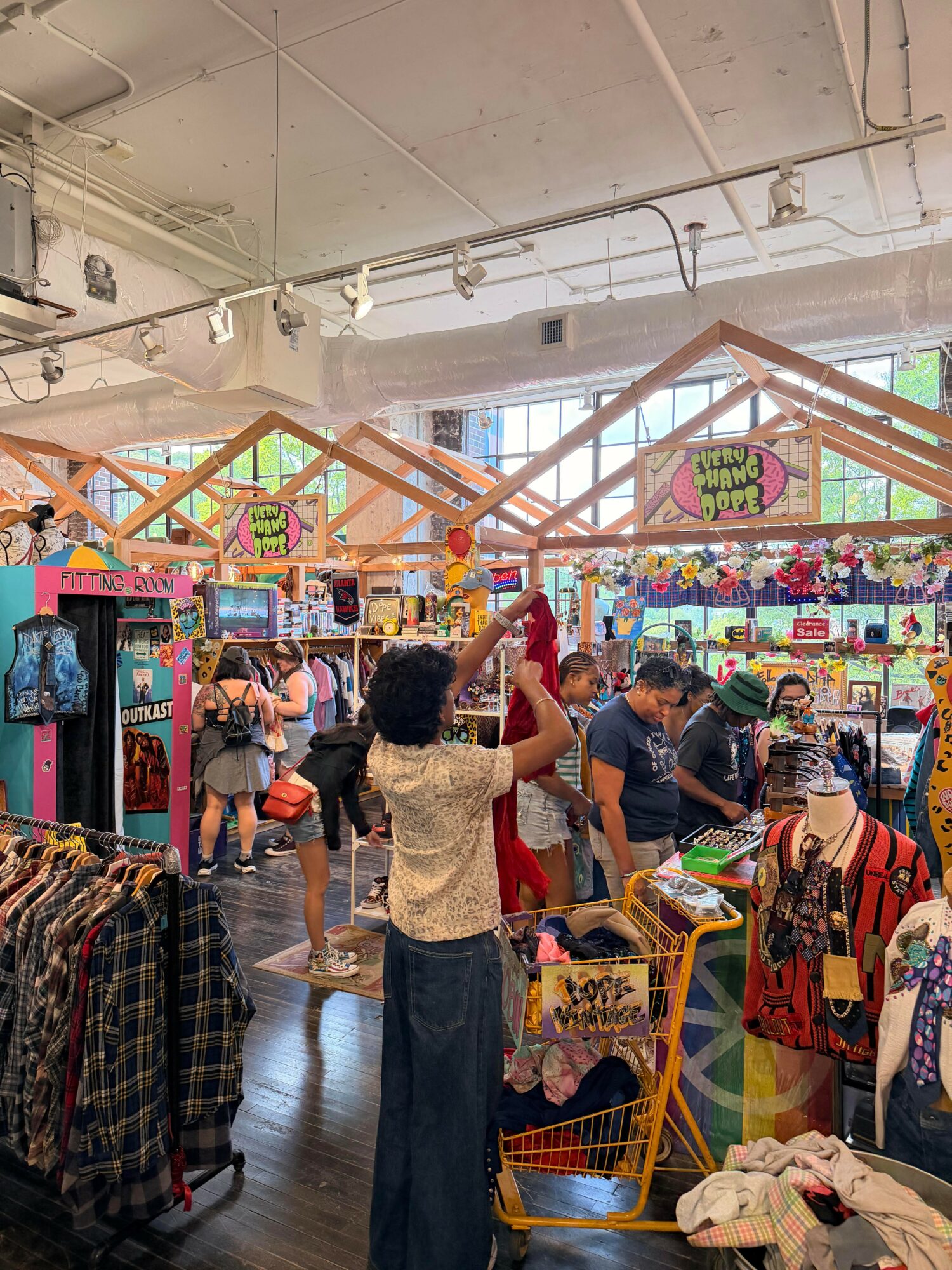 People shopping in a colorful store with clothing and toys, bright decorations, and large windows, inside a well-lit retail space.