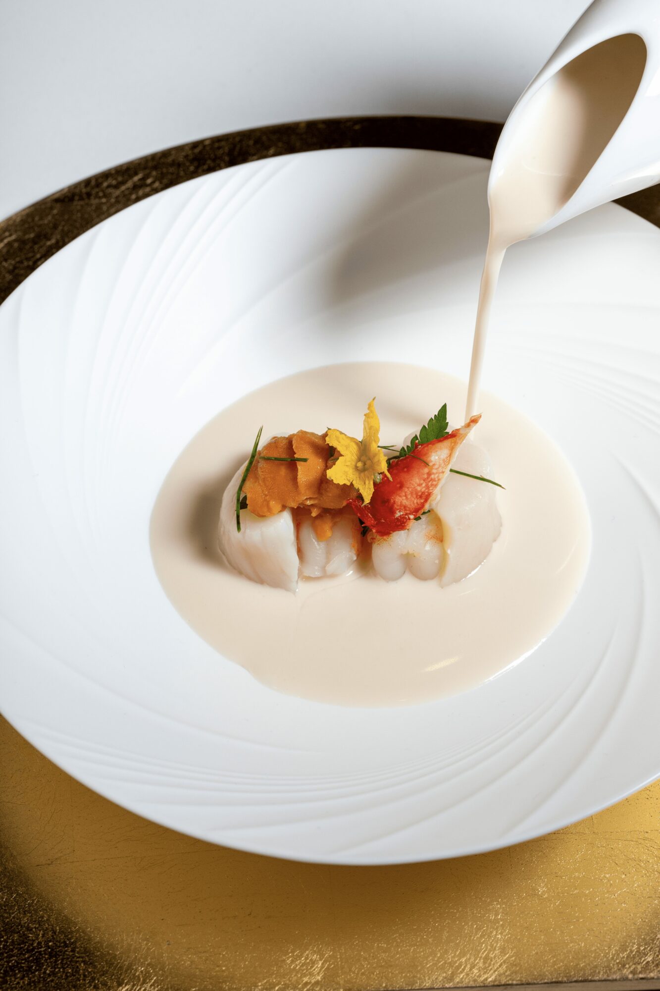 Cream being poured over a plated dish with vegetables and garnishes on a white plate.