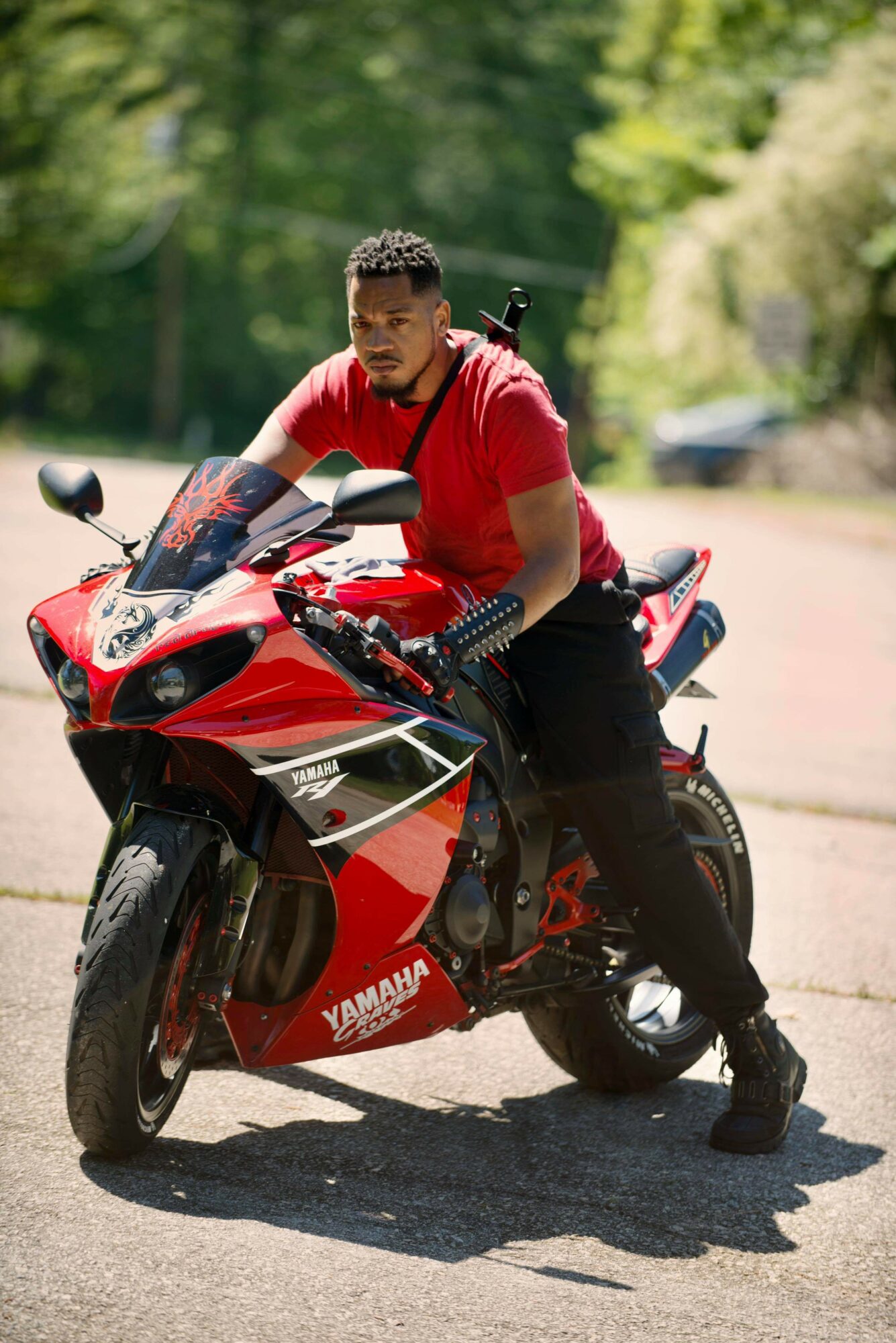 Young man in red shirt sitting on a red Yamaha motorcycle outdoors on a sunny day.