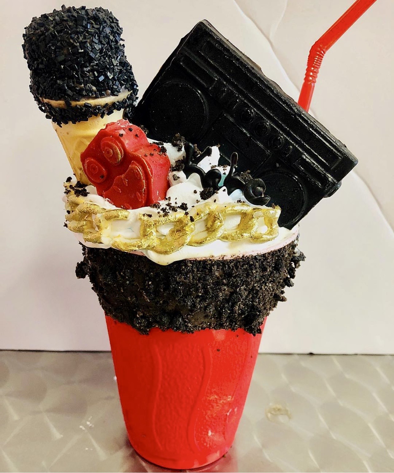 A dessert with ice cream, candy, and a drink in a red cup, topped with various sweets and a straw.