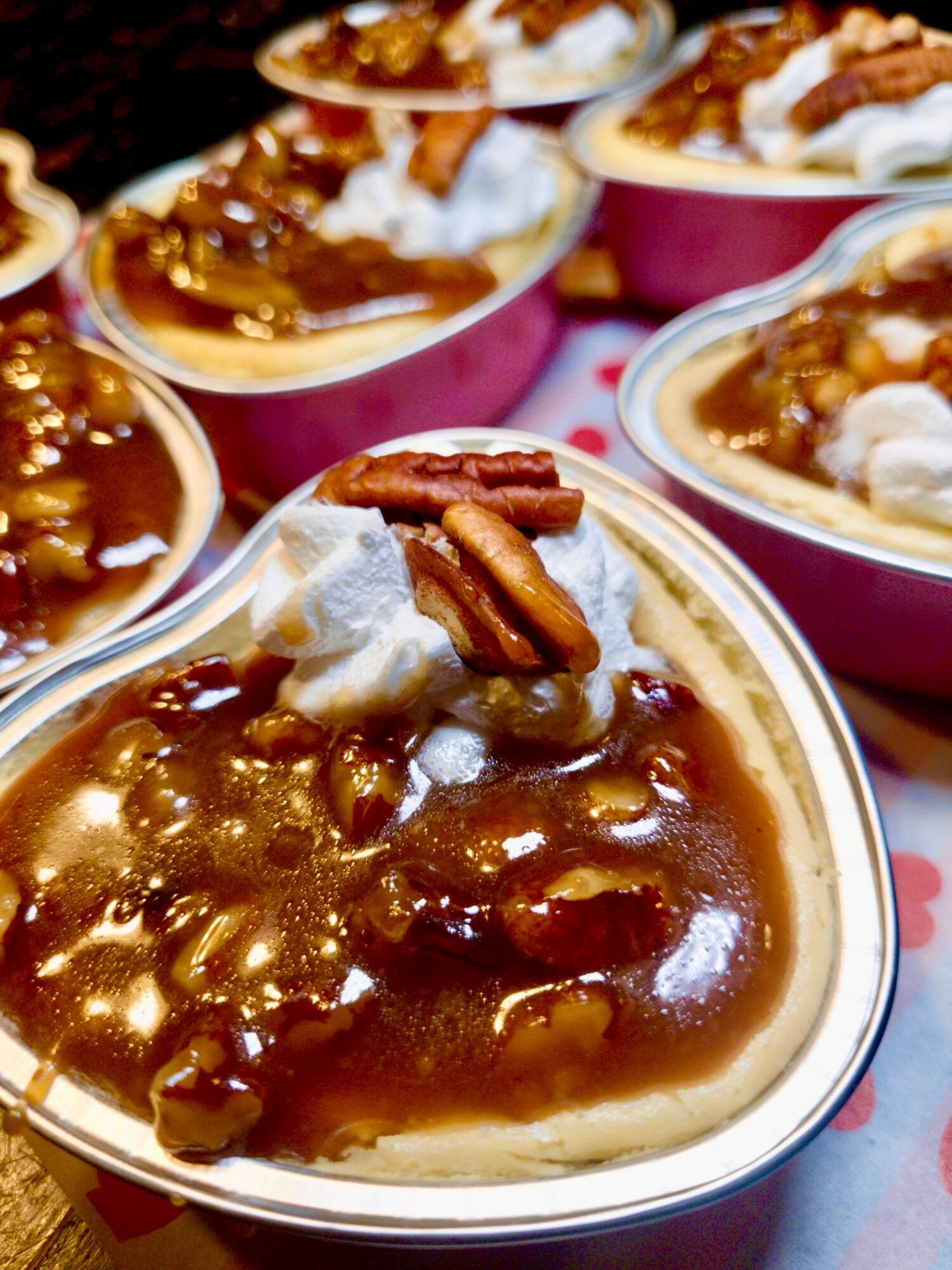 Multiple bowls of caramel pudding topped with whipped cream and pecans, arranged on a table.