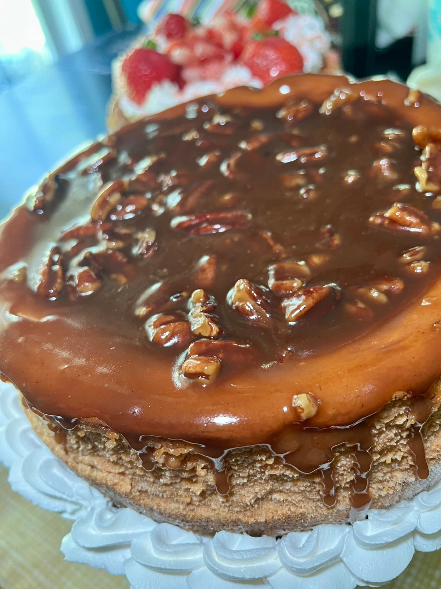 Chocolate cake with caramel topping and chopped nuts on a decorative white plate.