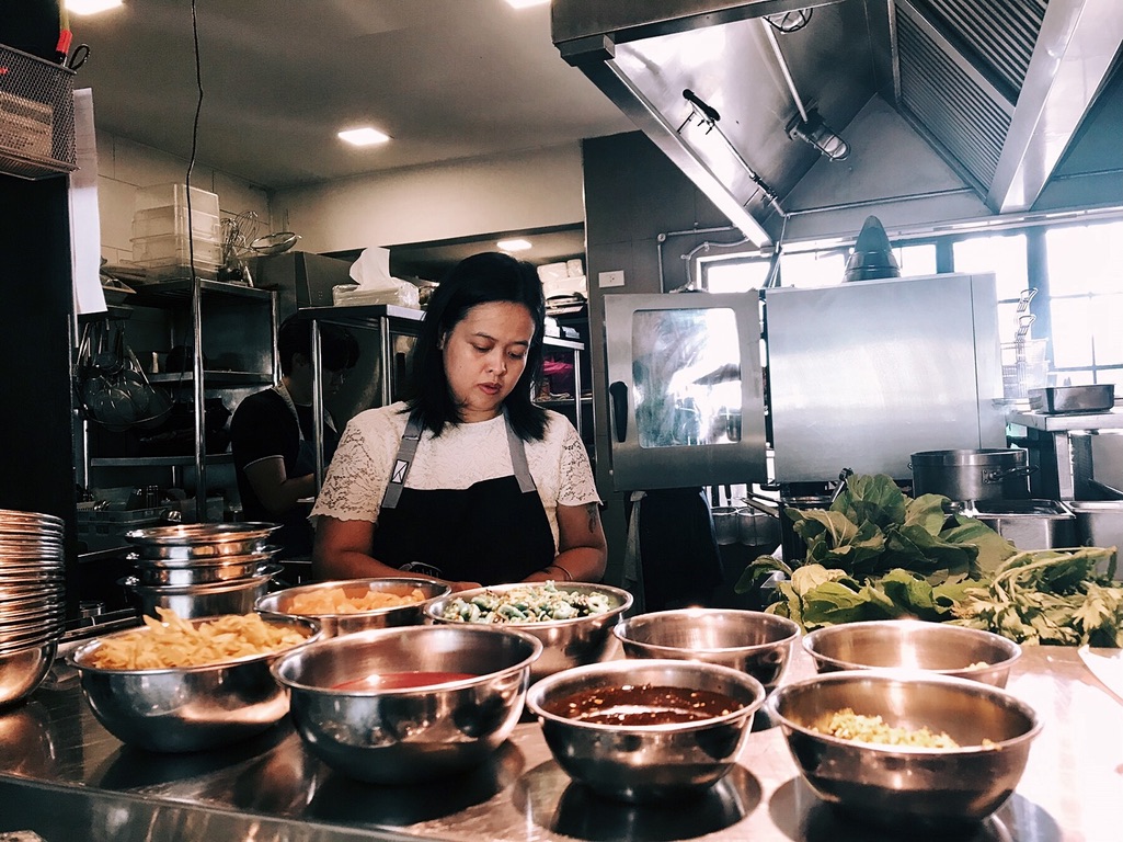 Woman in a kitchen preparing food with bowls of ingredients in front of her.