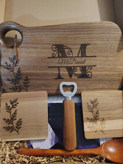 Wooden cutting board with engraved initials and floral designs, two small wooden blocks, a bottle opener, and a spoon.
