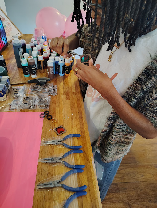 Person with dreadlocks and a scarf, standing at a table with nail polish bottles, tools, and pink balloons.
