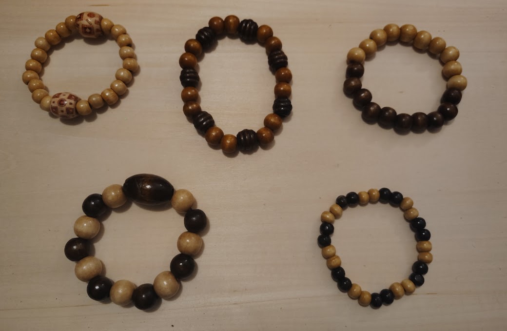 Five beaded bracelets arranged on a light surface, each with different bead colors and sizes.