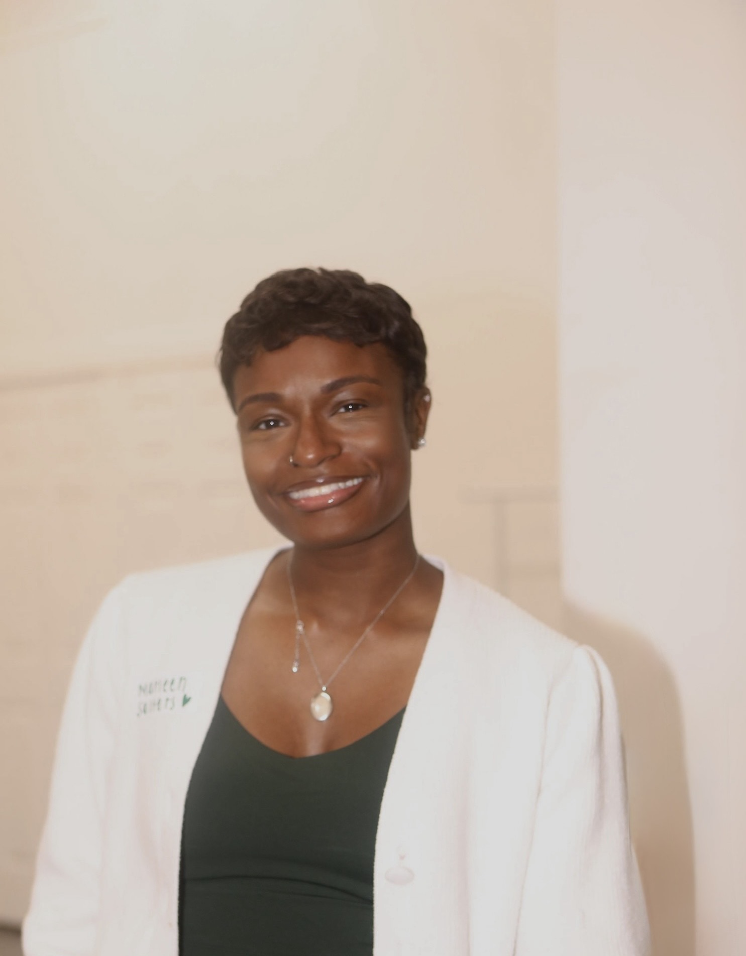 Portrait of a woman with short curly hair wearing a white blazer and dark top, smiling, against a plain background.