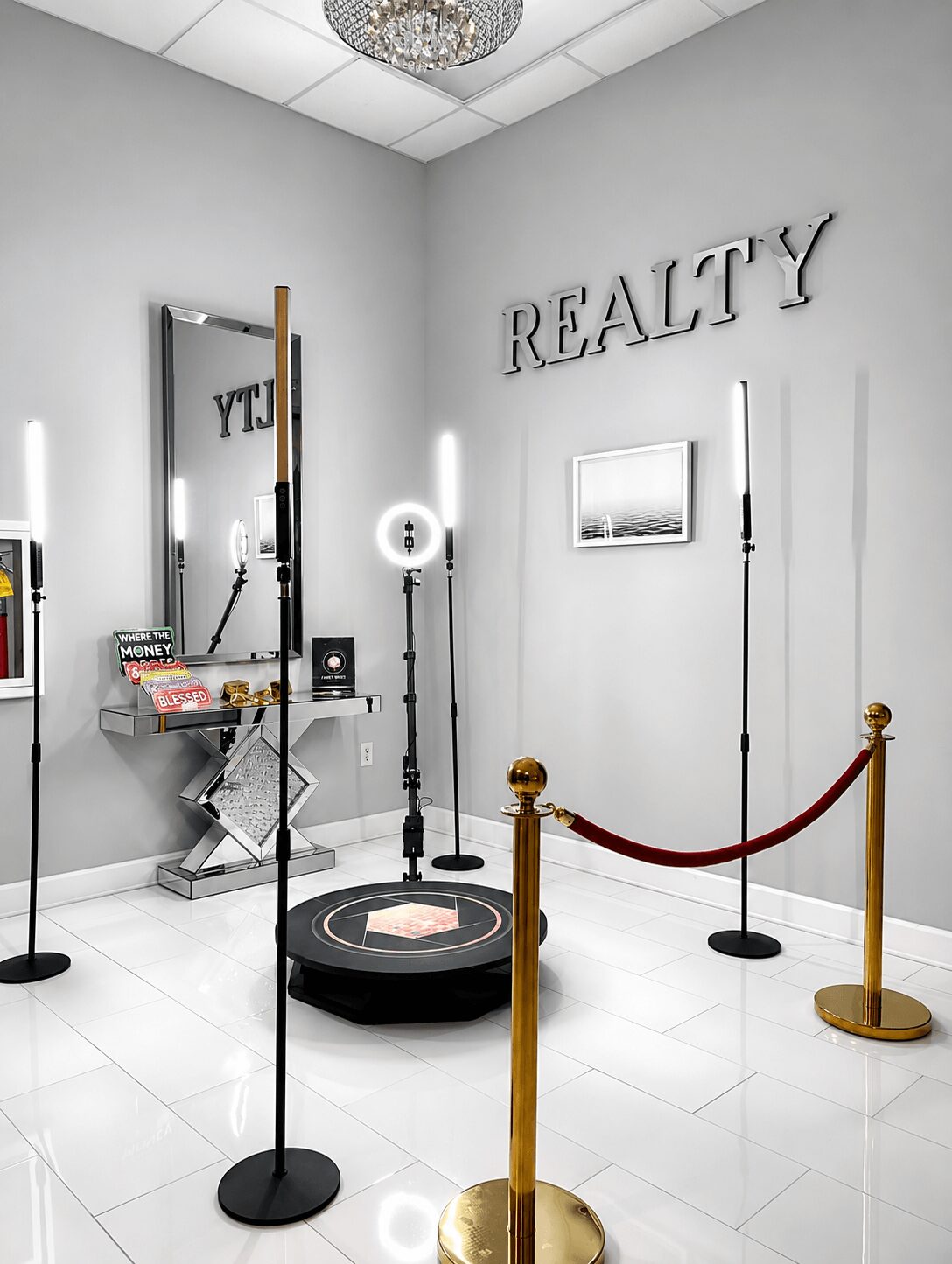 Room with a mirror, a small table, and a robotic device on a circular platform, with a sign reading 'REALTY' on the wall.