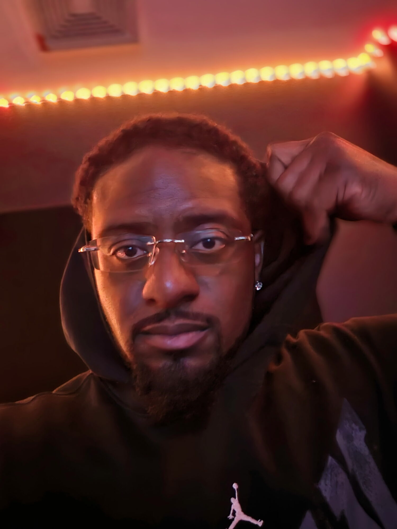 Person with glasses and a beard, raising a fist, in a dimly lit room with orange LED lights.