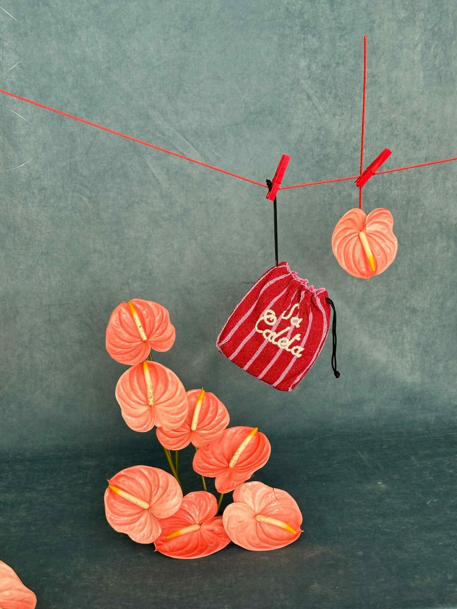 A red and white striped drawstring bag surrounded by orange and pink flower petals on a green surface.