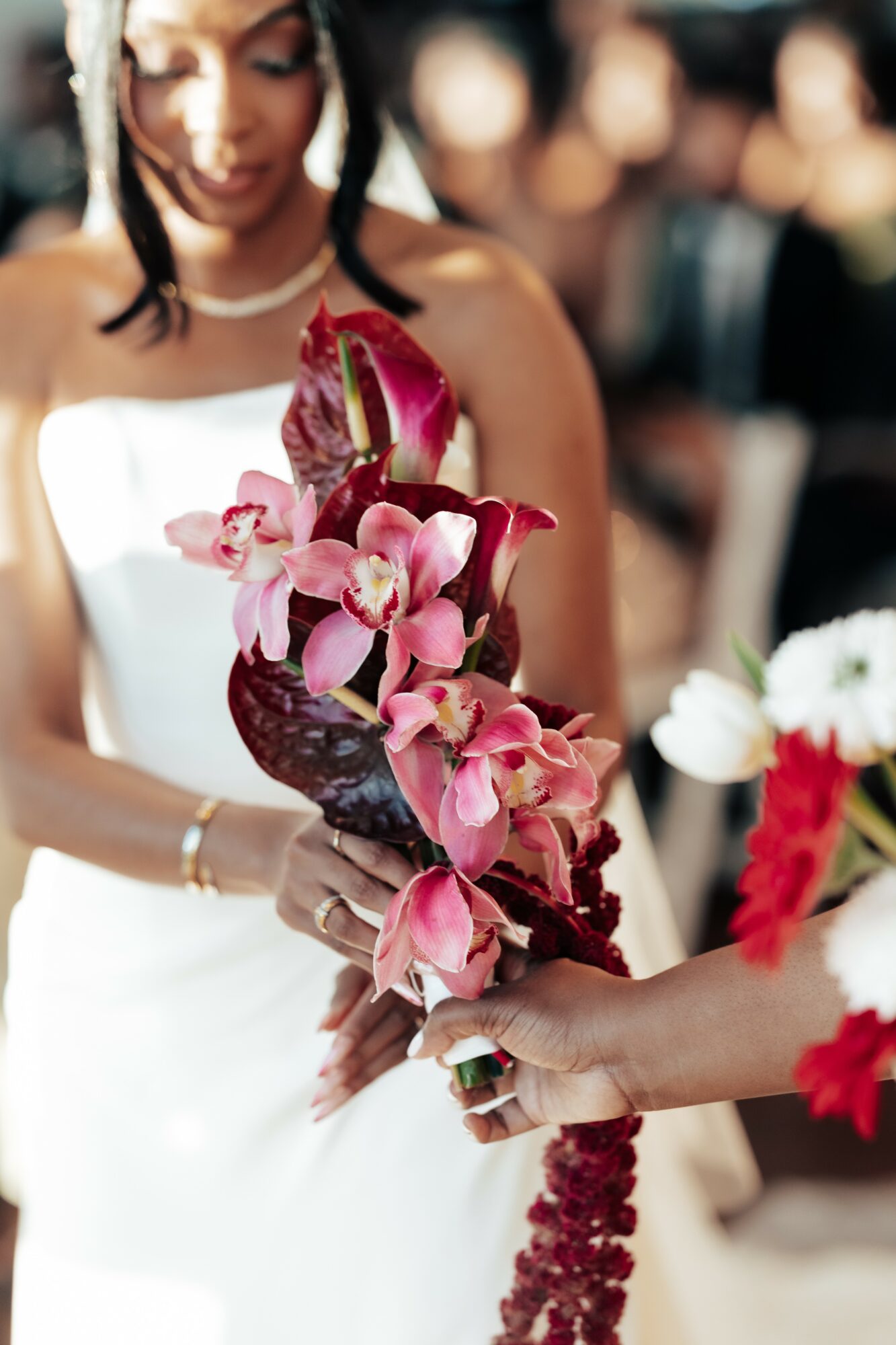 Person in white dress holding a bouquet of pink orchids and red flowers, with blurred background.