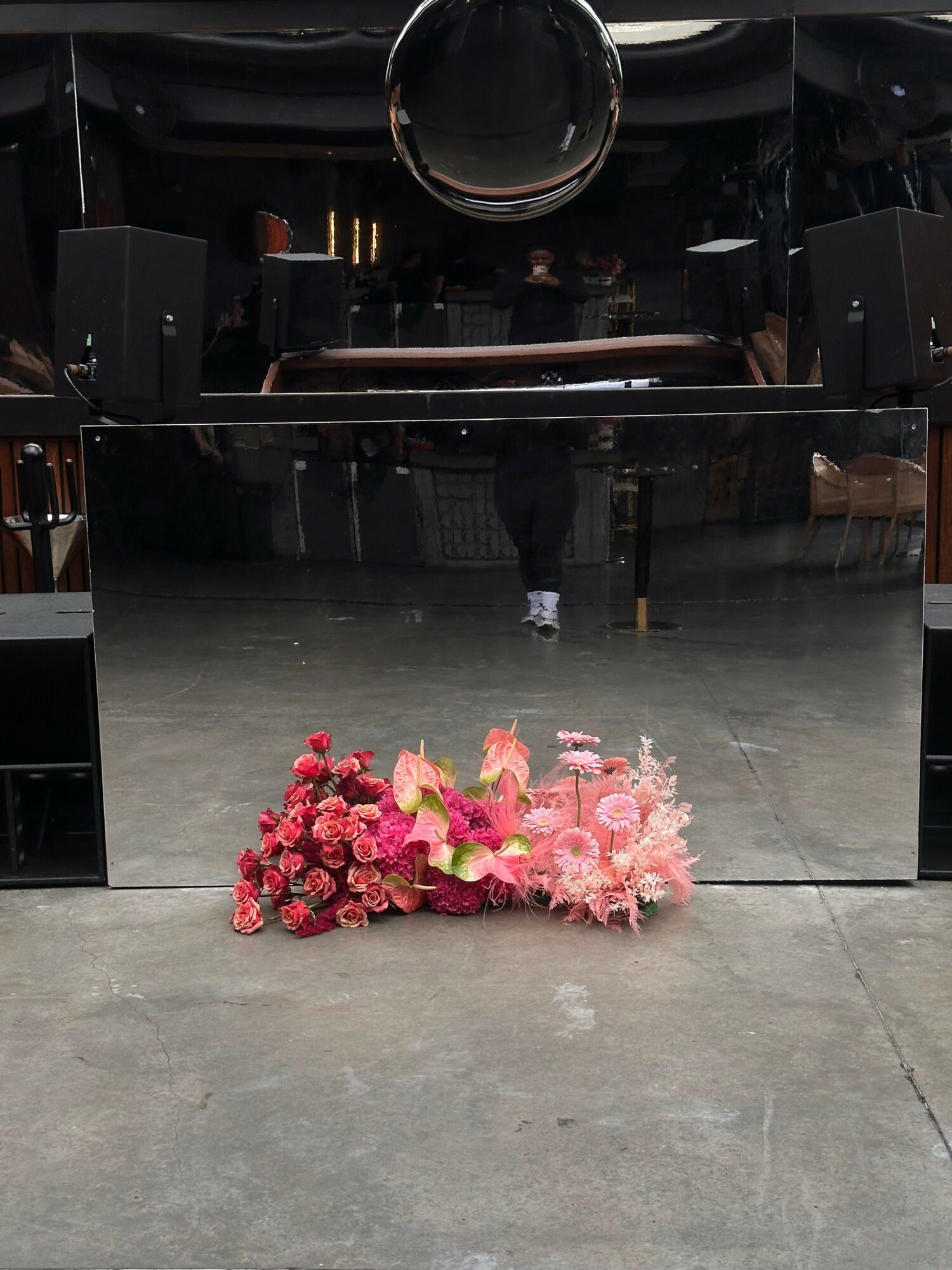 Pink and red flower arrangements on a concrete floor in front of a black piano, with a person in the background.