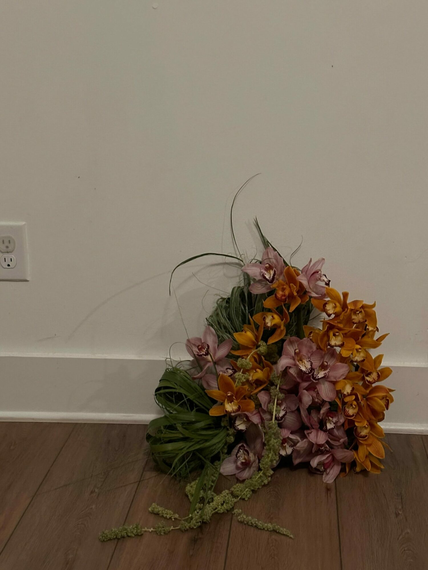 A bouquet of flowers with pink, orange, and green leaves on a wooden floor against a white wall.